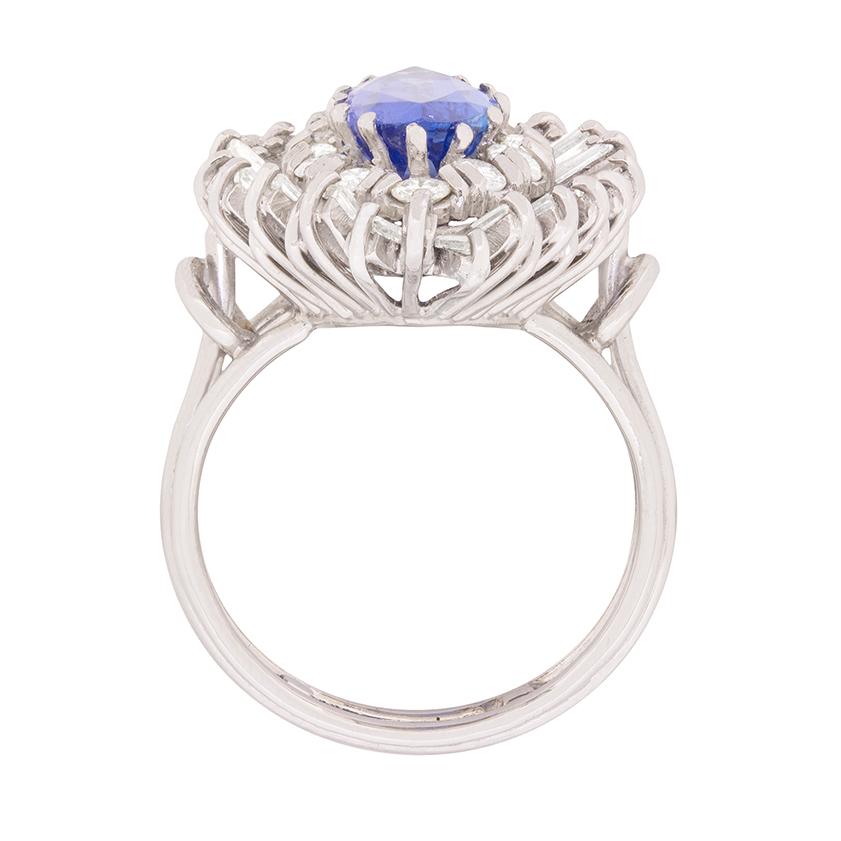 This captivating 1970s cocktail ring is destined to become a signature piece!

This vintage ring stars a 2.46 carat, electric blue, marquise-shaped tanzanite claw set at the centre of a twelve diamond halo. A further thirty-eight baguette cut
