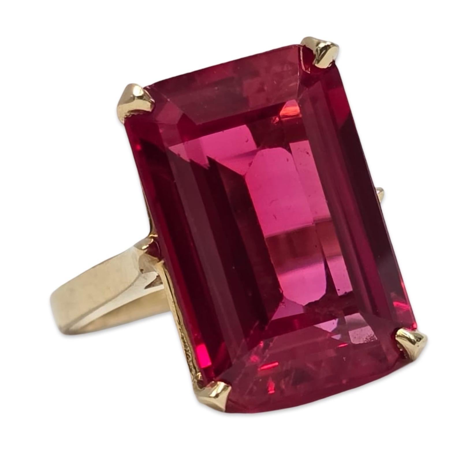 Une bague de cocktail vintage remarquable en or massif 14 carats, sertie d'une pierre précieuse exceptionnelle de couleur rouge rubis, taillée en émeraude, d'une présence imposante. La pierre présente une teinte cramoisie saturée, une excellente