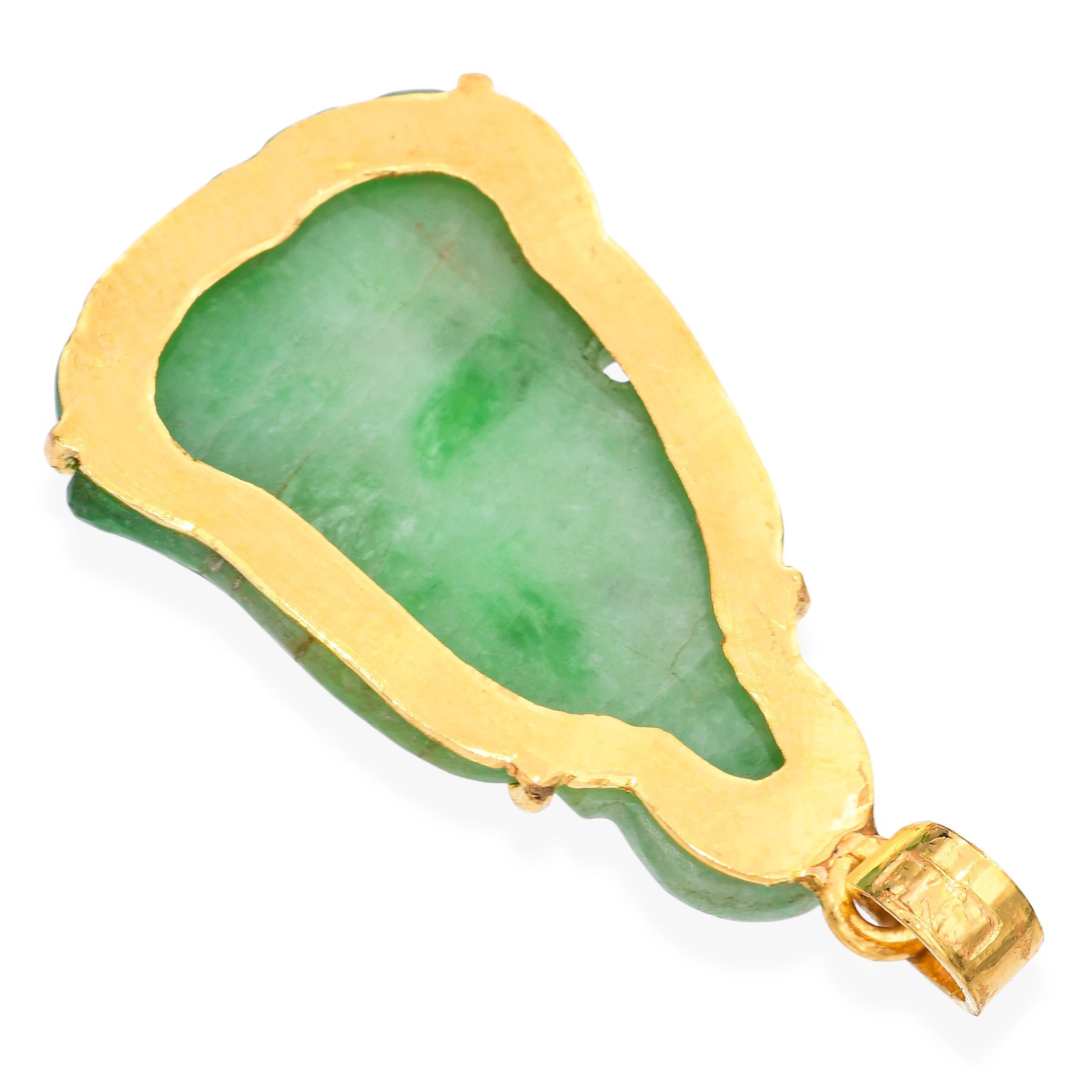Pendentif vintage en or jaune 24k présentant une pièce centrale en jade magnifiquement sculptée avec des détails complexes. La riche monture en or pur met en valeur la beauté naturelle du jade, créant un contraste saisissant entre les tons chauds de
