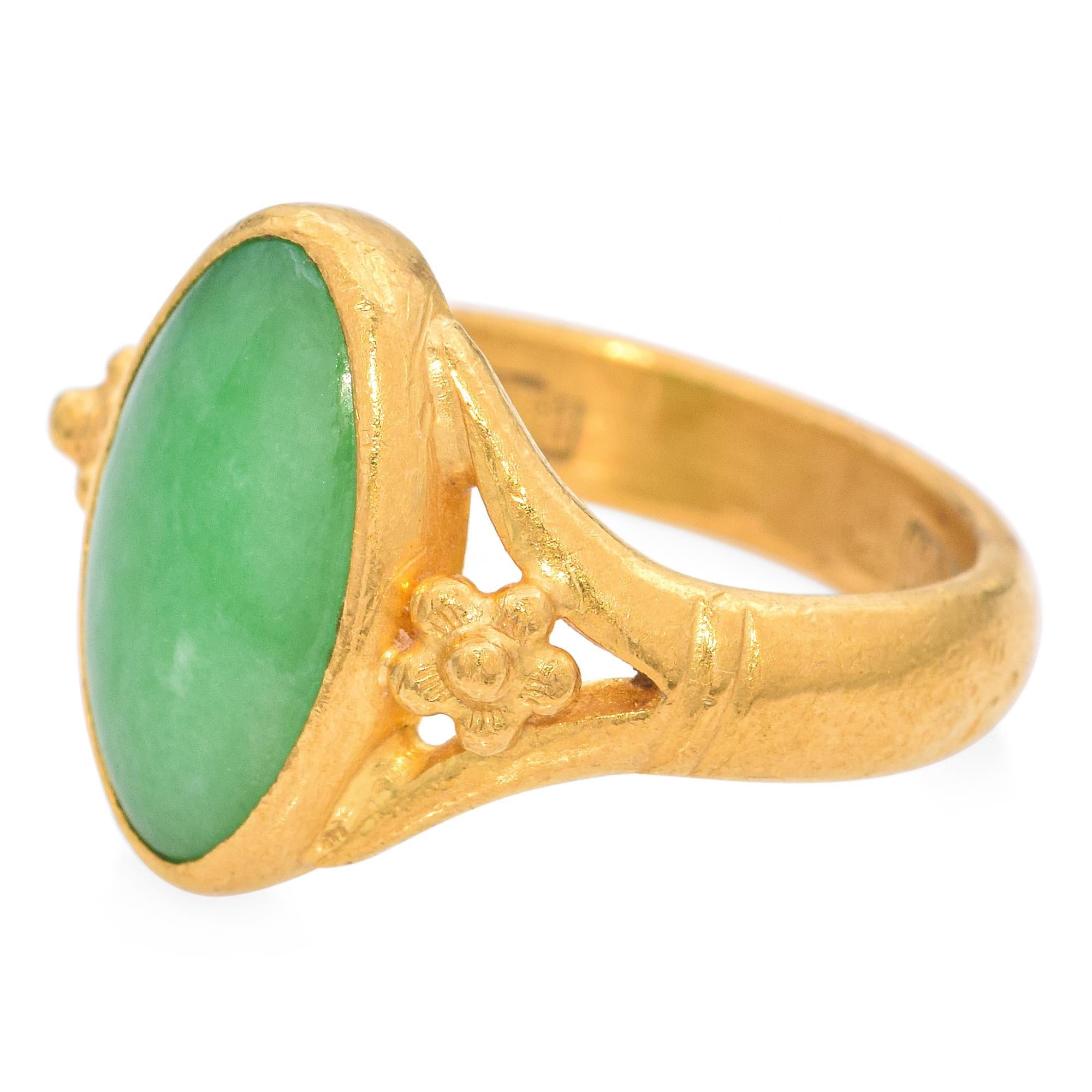 Une bague raffinée et élégante mettant en valeur un jade taillé en cabochon d'un vert éclatant. La bague est fabriquée en or jaune 24 carats et présente des détails complexes sur la bande qui complètent la pièce centrale en jade. Cette bague exquise