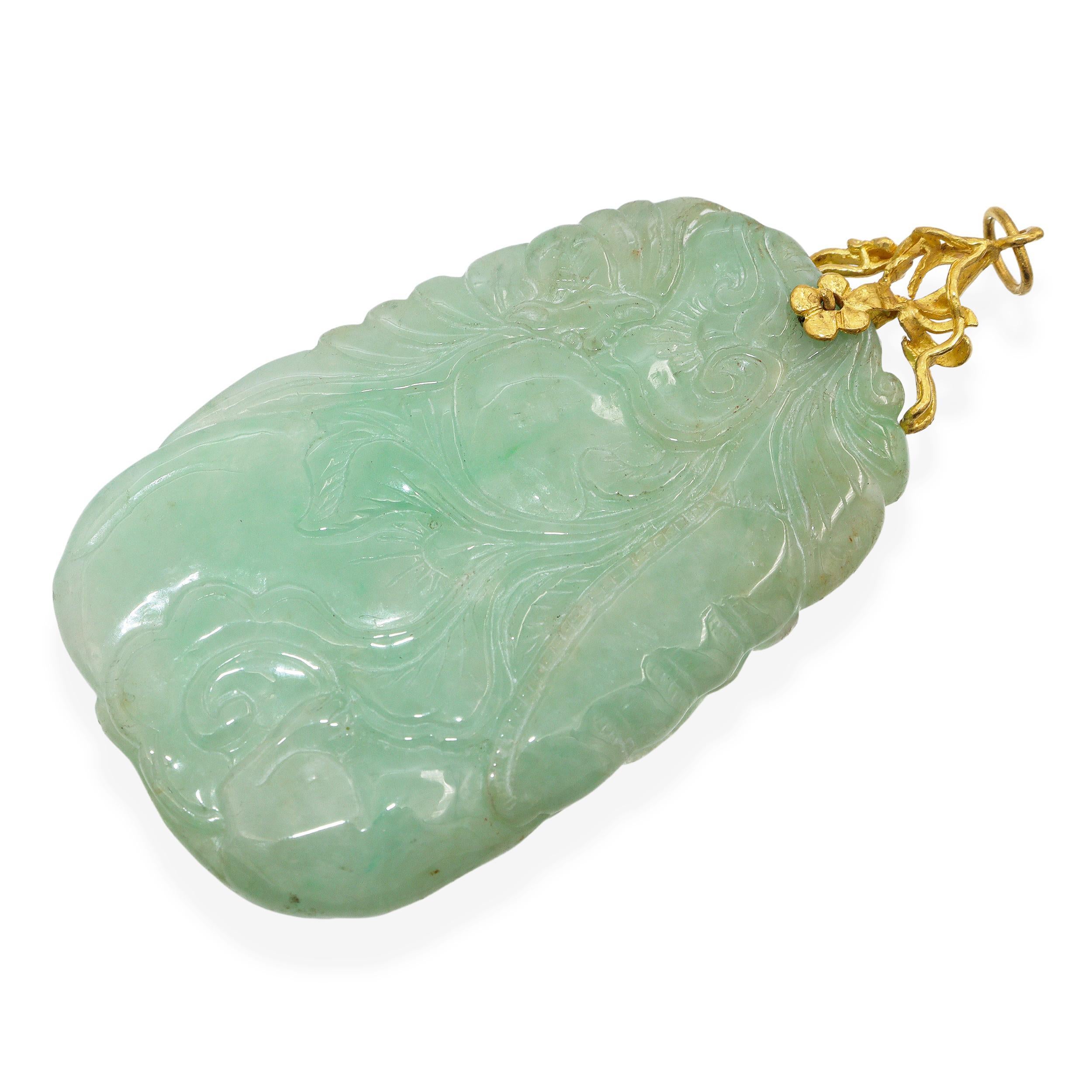 Questo elegante ciondolo presenta una splendida placca di giada intagliata a mano, graziosamente ornata da una delicata coda floreale in oro giallo 24 carati. La giada presenta una tonalità verde morbida e traslucida con variazioni naturali,