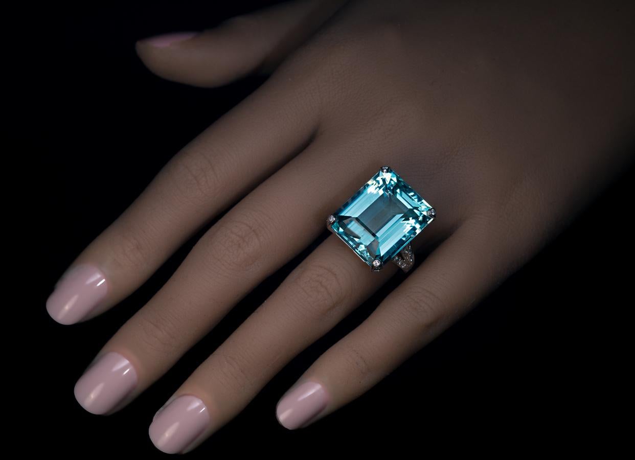 This diamond encrusted white 18K gold ring features an emerald cut aquamarine of a beautiful ocean blue color and excellent saturation.
The aquamarine measures 19.71 x 16.62 x 11 mm and is approximately 25.04 cts.
The ring is marked with maker’s