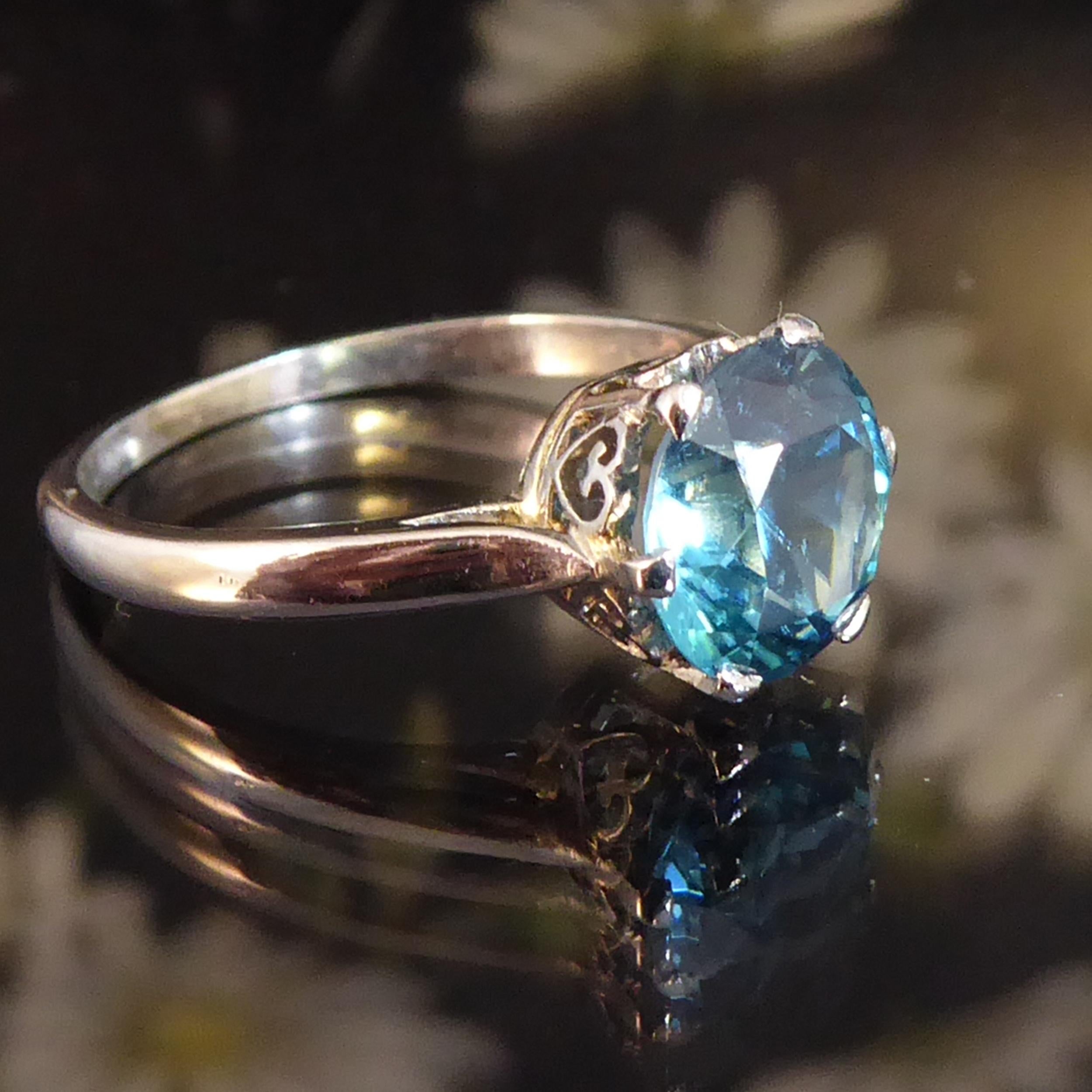 A vintage solitaire ring set with a round mixed cut blue zircon of vivid blue and with good clarity.  The zircon weighs 2.50 carat and is held within eight white claws, to an open, pierced mount decorated with heart shape supports all around.  The