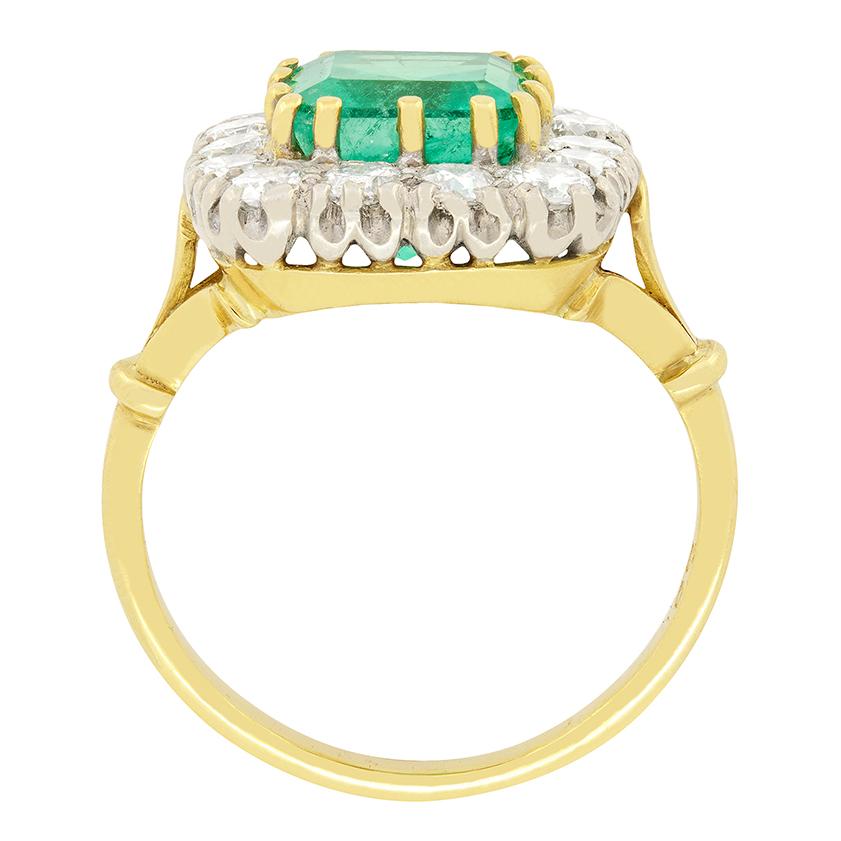 A lustrous 2.60 carat Emerald features central to this vintage cluster ring. The emerald cut stone has been firmly set in place with 18 carat yellow gold claws. The surrounding halo features 14 round brilliant diamonds, totalling to 0.70 carat. The