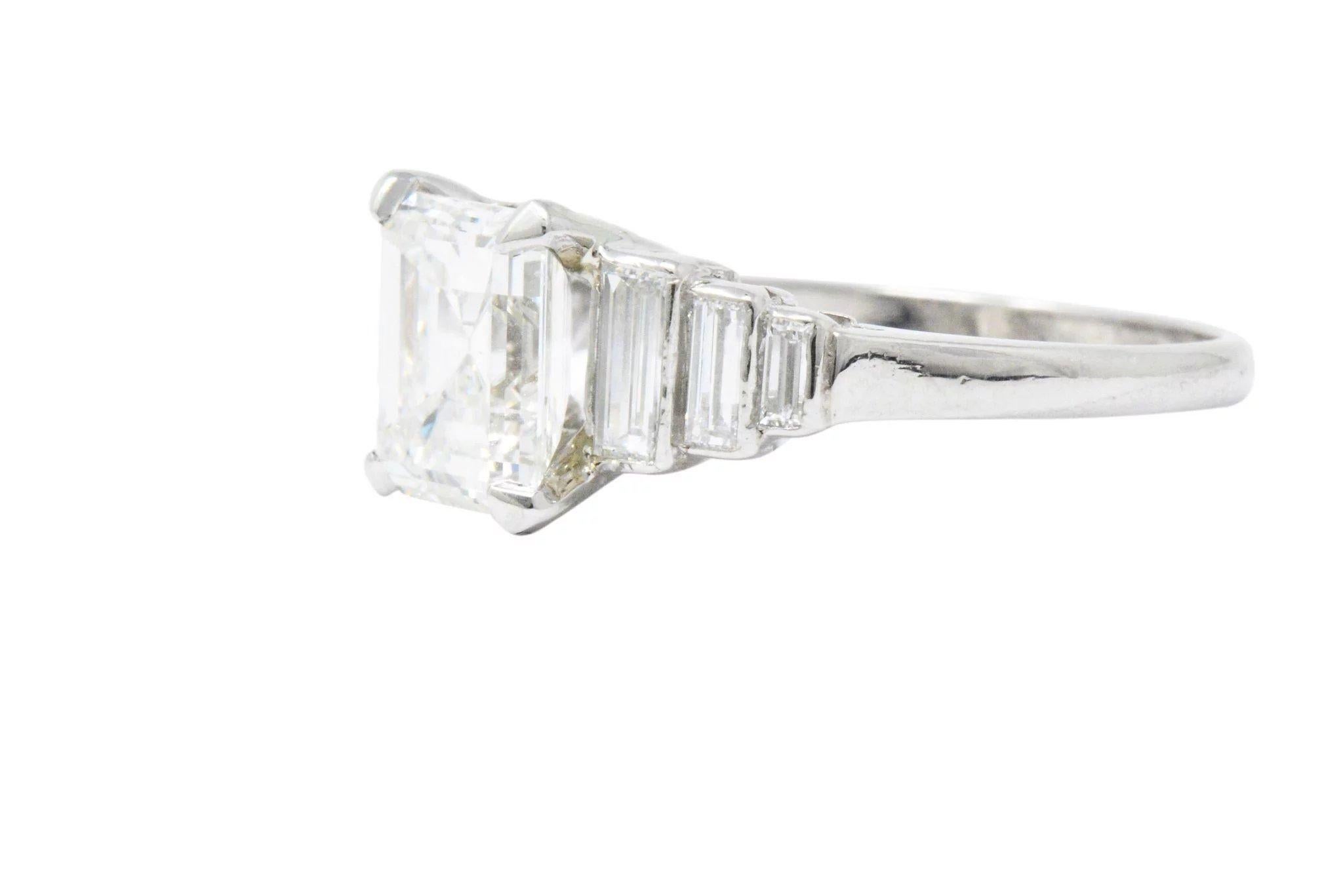 Centering an emerald cut diamond weighing 2.11 carats, I color and VS1 clarity, accompanied by GIA Diamond Grading Report

Flanked by three graduated, bezel set baguette cut diamonds on each side, approximately 0.60 carats total, GHI color and VS