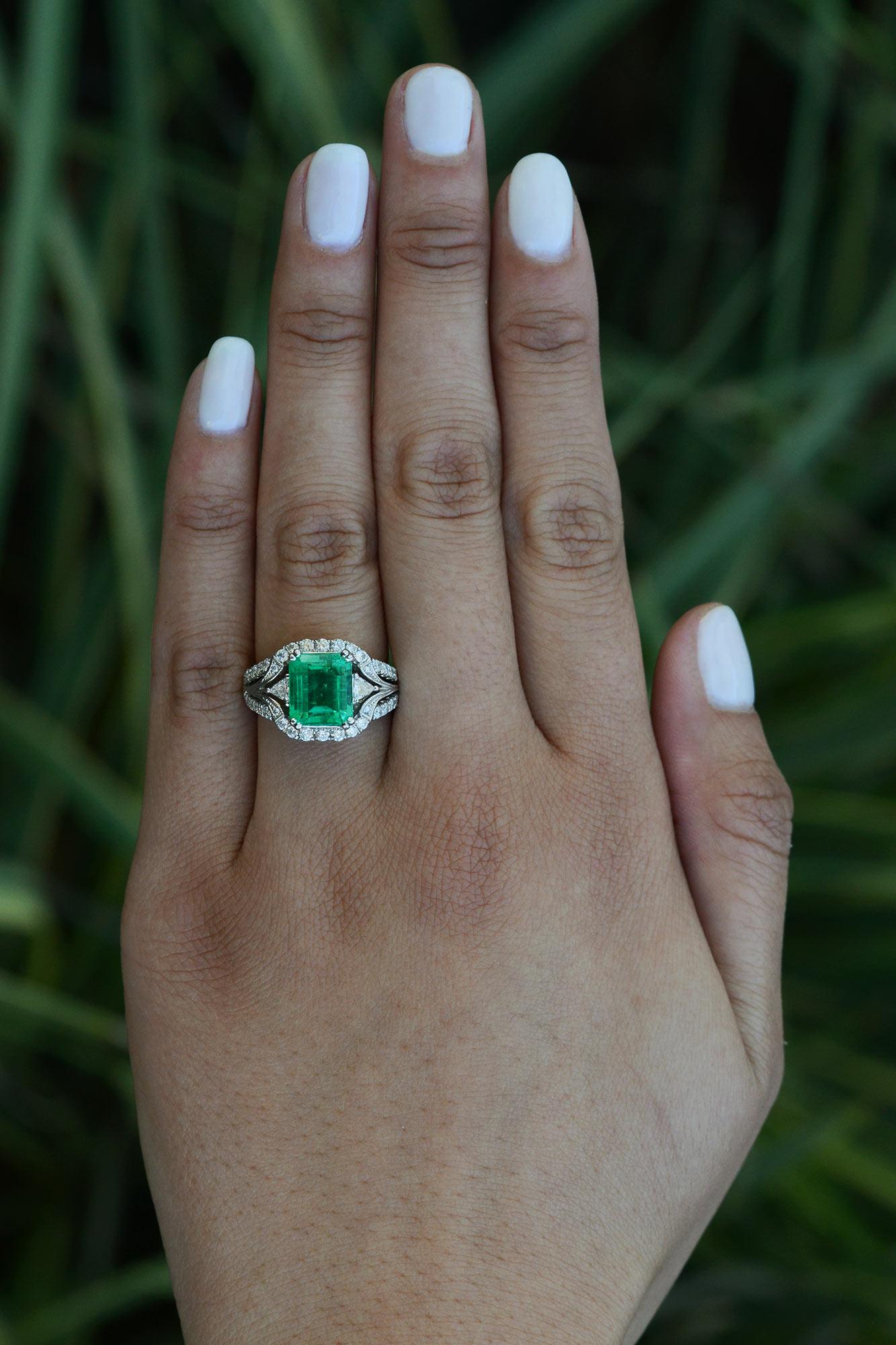 A magnificent emerald is exhibited in this vintage 18k white gold ring. Displaying a ravishing bright tone peering out of over 1 carat of prominent diamonds all showcased in a notable openwork design. The 1980s were a pivotal time for jewelry and