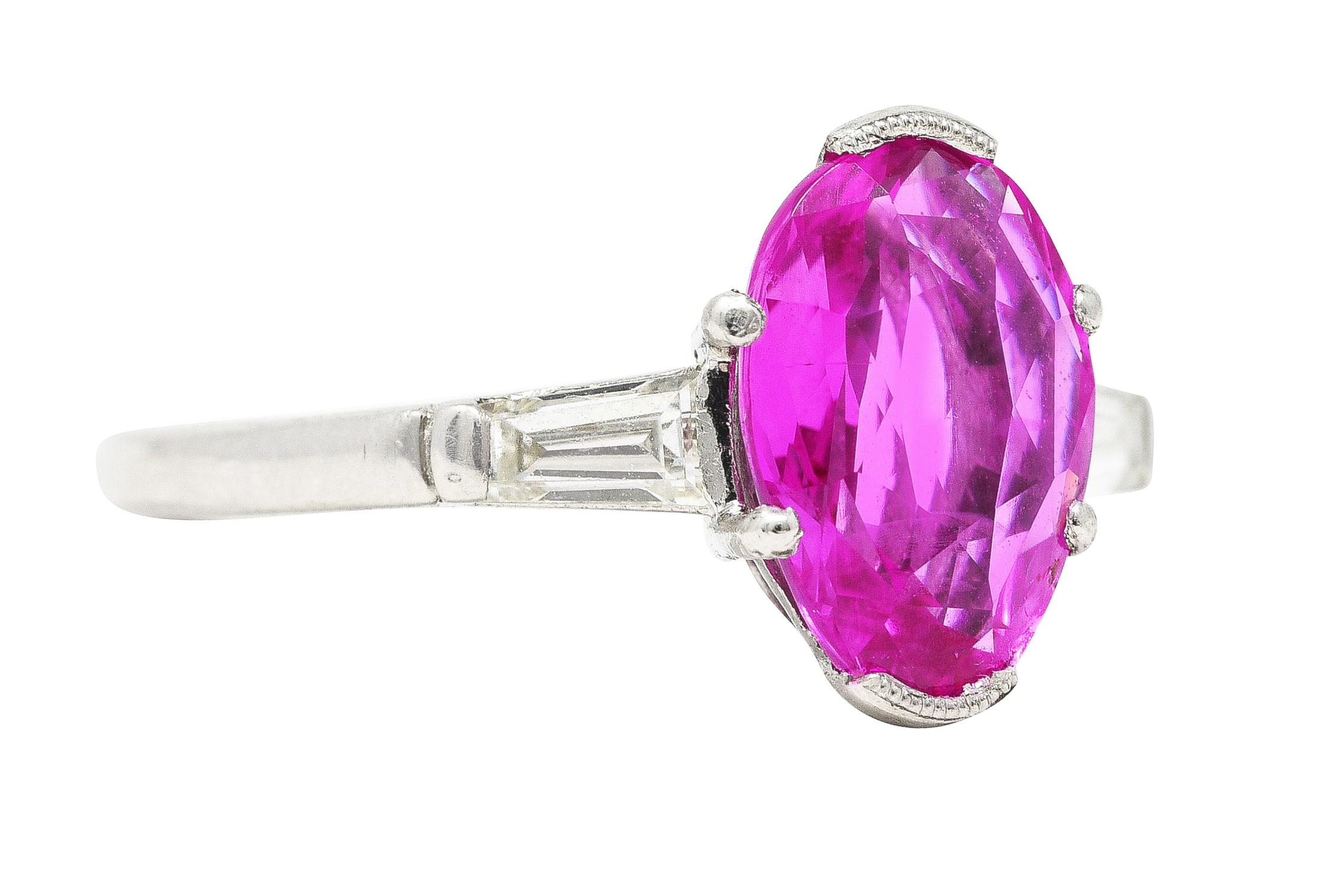 Featuring a mixed oval cut pink sapphire weighing 2.53 carats. Transparent purple pink with no indications of heat. Half bezel set in a stylized basket and flanked by bar set tapered baguette cut diamonds. Weighing in total approximately 0.30 carat