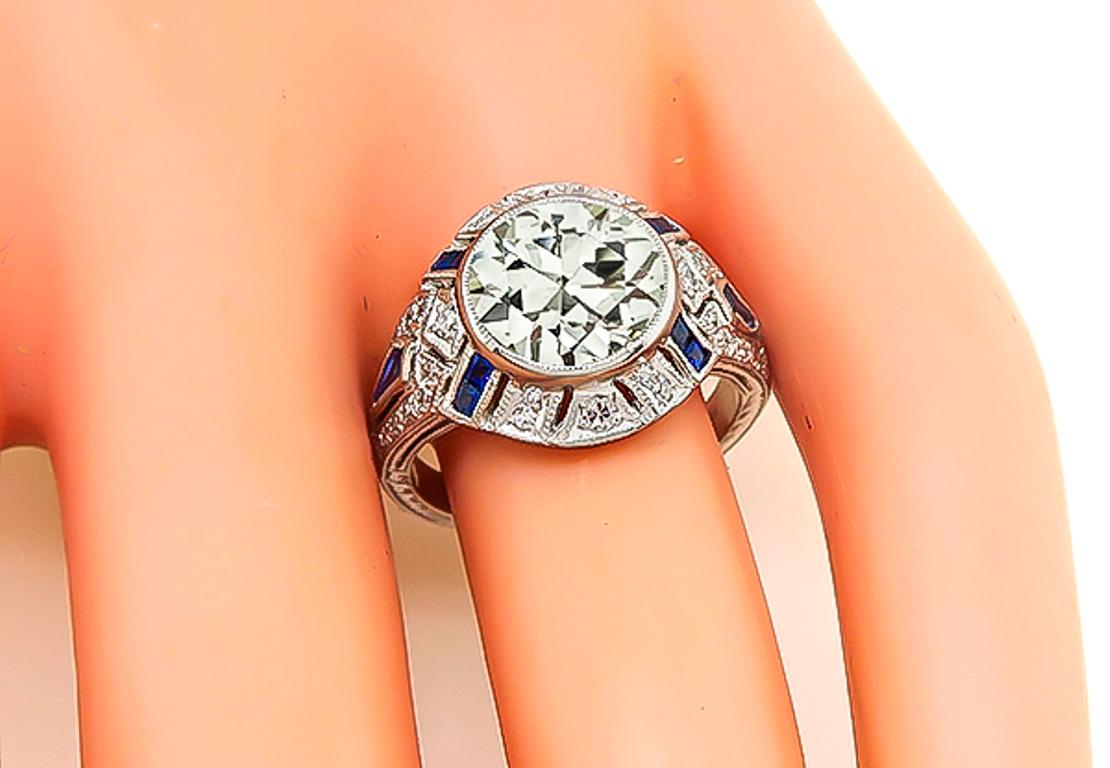 This fabulous platinum engagement ring from the Art Deco era is centered with a sparkling old mine cut diamond that weighs approximately 2.90ct. graded J color with I1 clarity. The center diamond is accentuated by dazzling diamond and sapphire