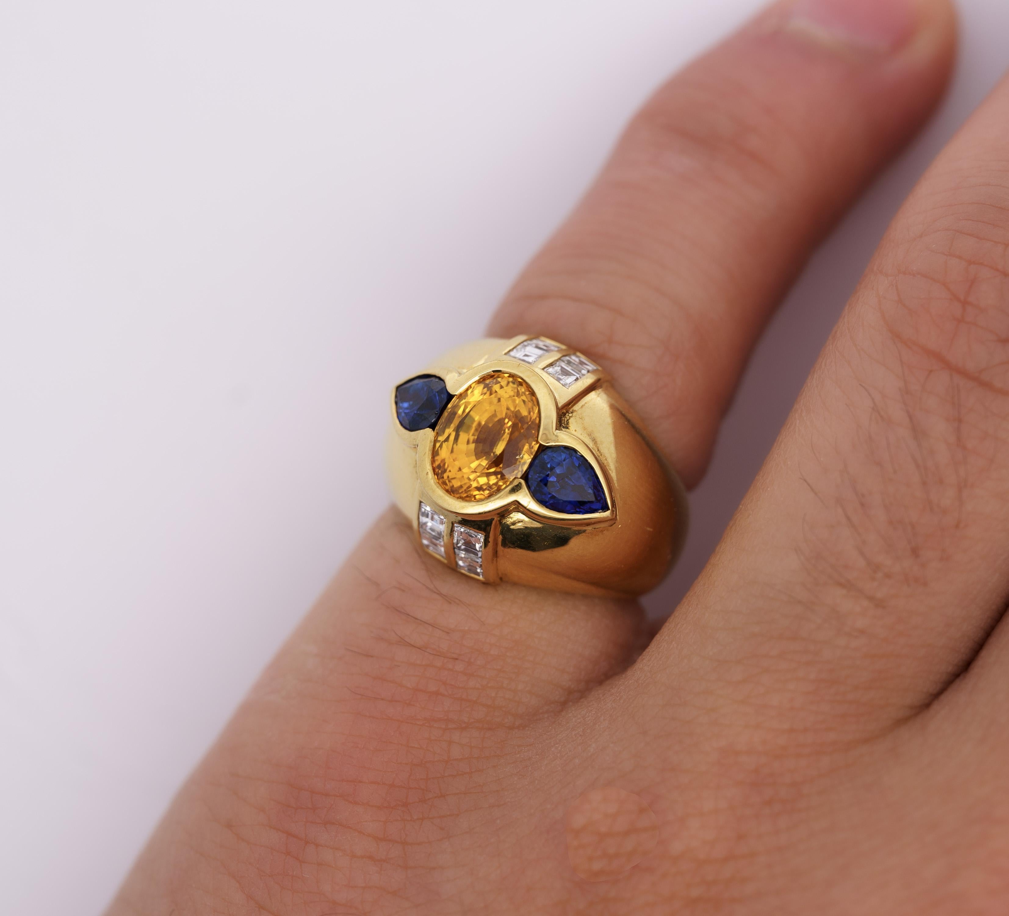 Anello a cupola vintage con zaffiro giallo, zaffiro blu e diamanti. 

Questo anello a cupola vintage è realizzato in oro giallo 18 carati. La pietra centrale è uno zaffiro giallo da 3 carati con taglio ovale. Ai lati della pietra centrale ci sono