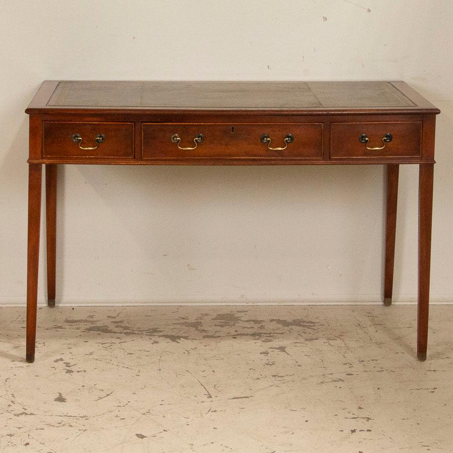 There is a reserved elegance to this mahogany writing desk from England. The clean lines, slightly tapered legs capped with brass feet and 3 smooth running drawers all add to the distinctive classic style of this desk. The sought-after vintage green