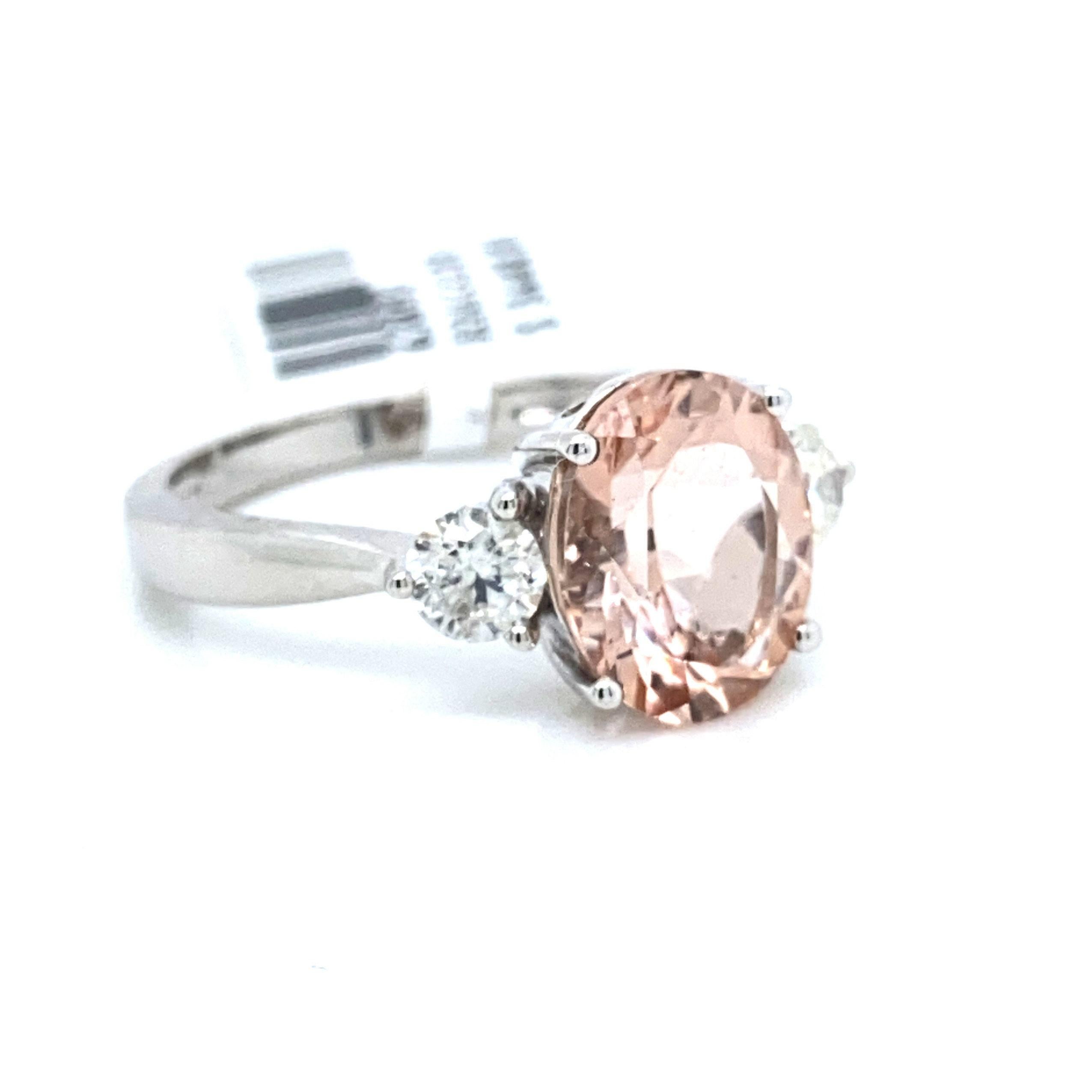 This is a majestic three stone morganite and diamond ring set in solid 14K white gold. The natural 3.36 Ct Morganite oval has an excellent peachy pink color and is complemented by a vivid diamond on each side. The ring is stamped 14K and is a true