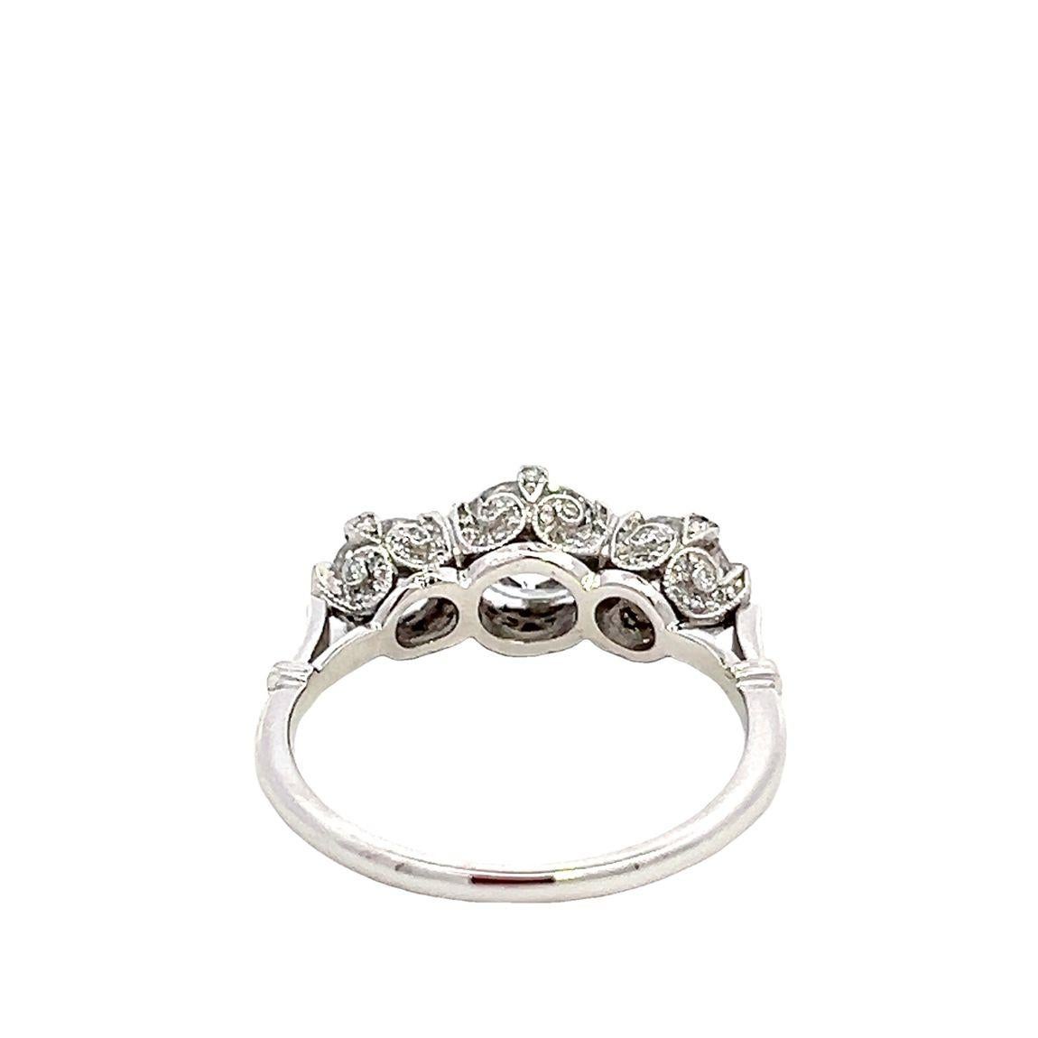 Anello di fidanzamento vintage in platino e diamanti con 3 pietre. La montatura in platino è incastonata con 69 piccoli diamanti a taglio rotondo, che racchiudono 3 diamanti rotondi a taglio brillante di colore H e purezza VS. Il diamante centrale è