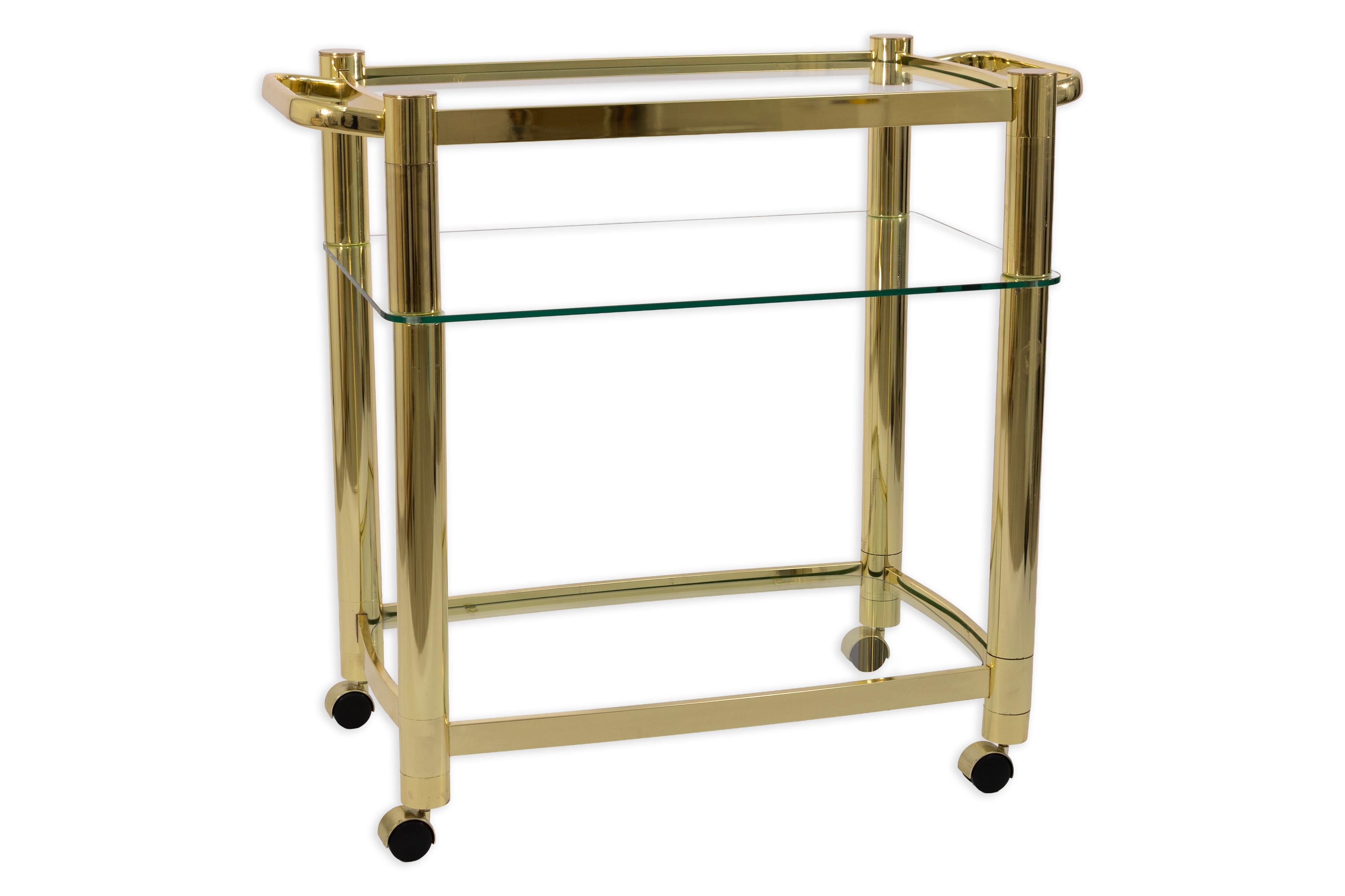 Add a touch of glamour to your entertaining space with this stunning 3-Tier Hollywood Regency Brass and Glass Rolling Bar Cart. Featuring a sleek and polished brass frame, this elegant cart is outfitted with three clear glass shelves and a mirrored