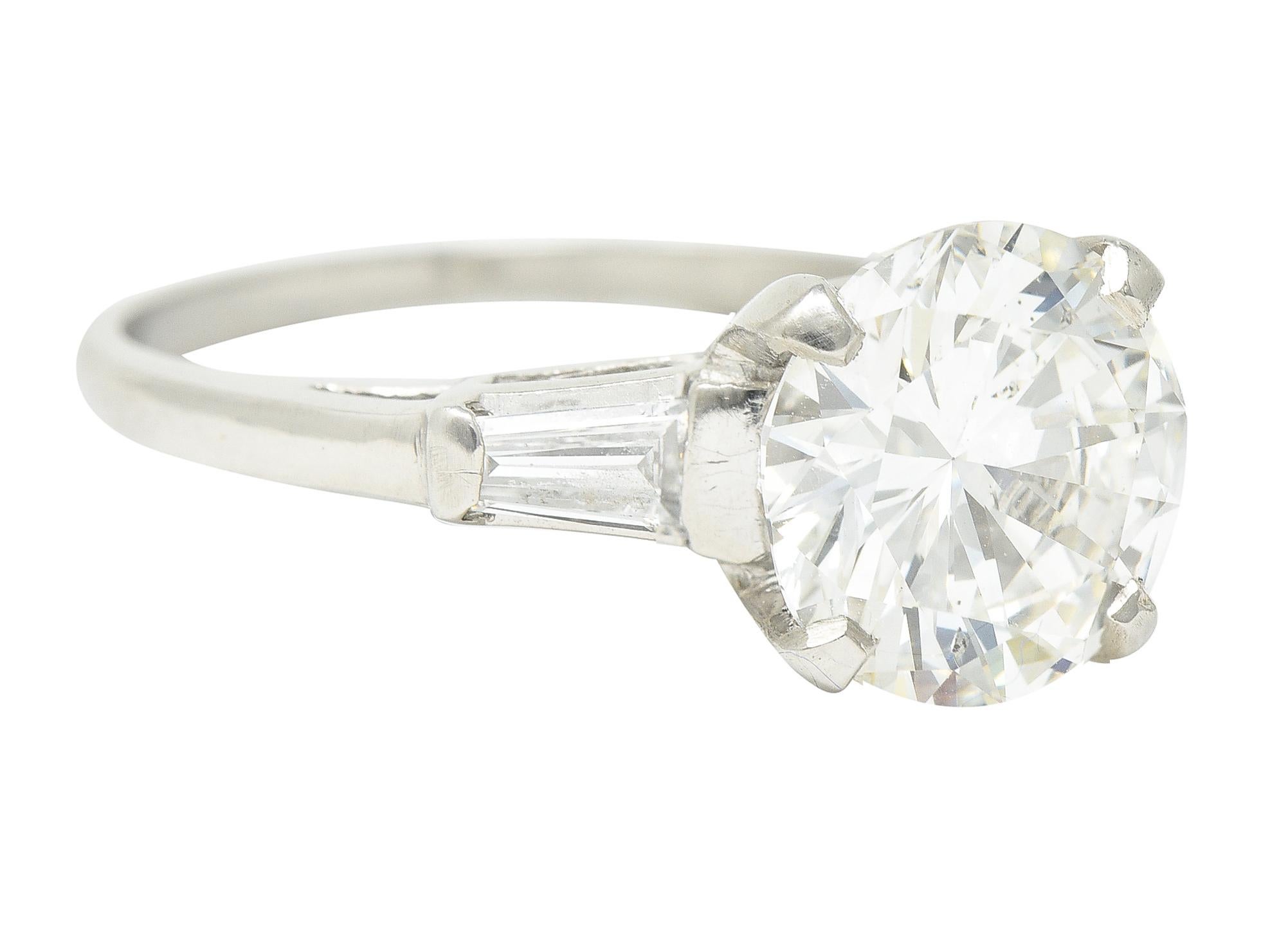 In der Mitte befindet sich ein runder Diamant im Brillantschliff mit einem Gesamtgewicht von 2,93 Karat - Farbe H und Reinheit SI2. Flankiert von kathedralenförmigen Schultern, die mit spitz zulaufenden Diamanten im Baguetteschliff besetzt sind. Mit