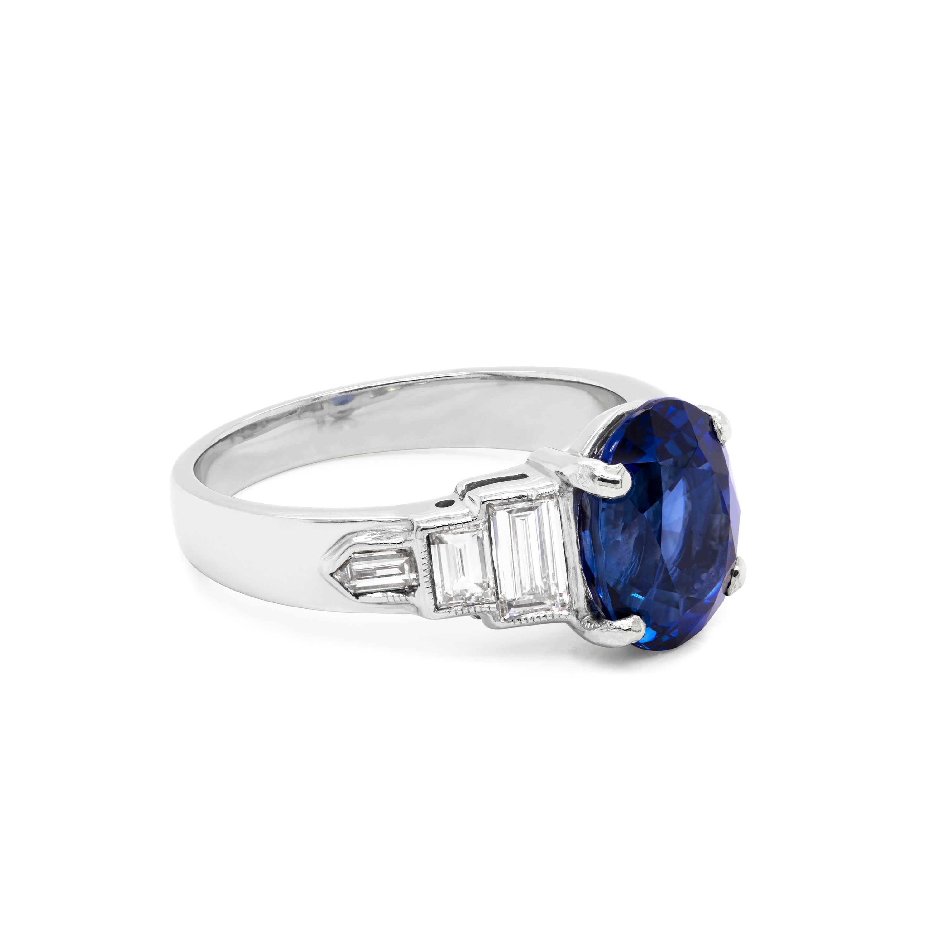 This beautiful Art Deco style, 1950's engagement ring features a natural royal blue oval sapphire weighing 3.18ct in a four claw open, back setting. The sapphire is accompanied by two step baguette cut diamonds and a bullet cut diamond on each