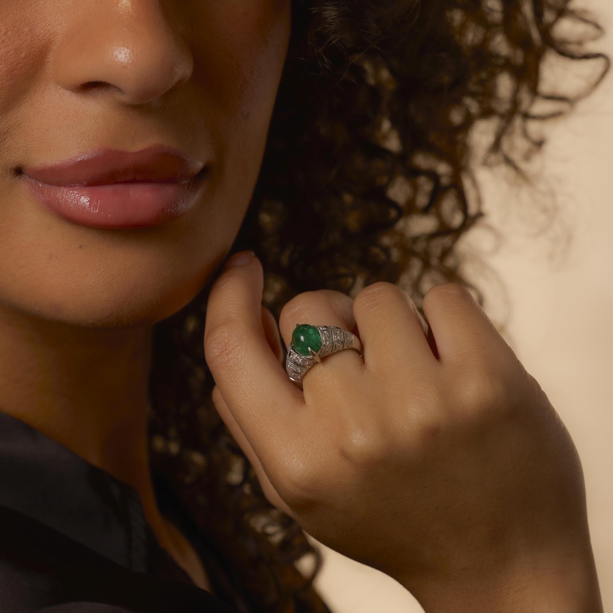 Este anillo vintage de los años 90 exhibe una vibrante esmeralda tallada en cabujón de 3,23 quilates, cuya superficie abovedada irradia un profundo color verde y un carácter natural. Alrededor de la piedra central hay treinta y seis diamantes