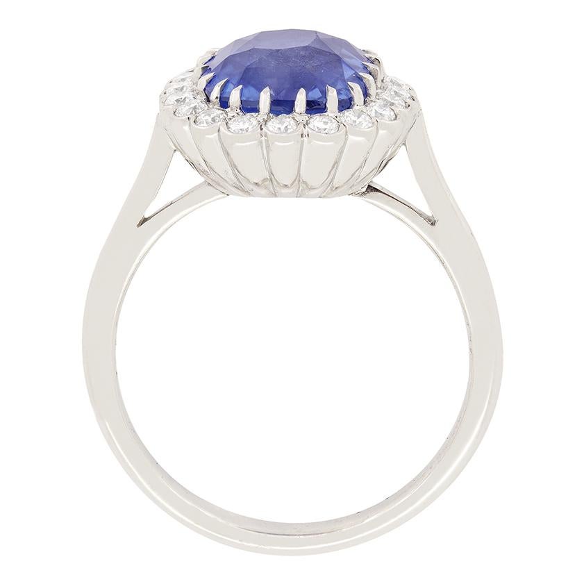 This glorious cluster ring boasts an awe inspiring Ceylon sapphire at its centre. The 3.70 carat stone is an old cushion cut and is completely natural and unenhanced. Enveloping the sapphire is halo of glistening round brilliant diamonds. These