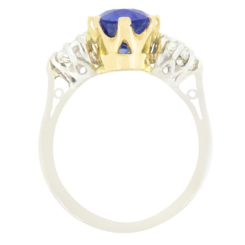 Un zafiro azul intenso se sitúa entre dos brillantes diamantes de talla antigua en este anillo trilogía vintage. El impresionante zafiro de 3,90 quilates es una piedra de talla oval, certificada como de Sri Lanka, natural y sin calentar. Los