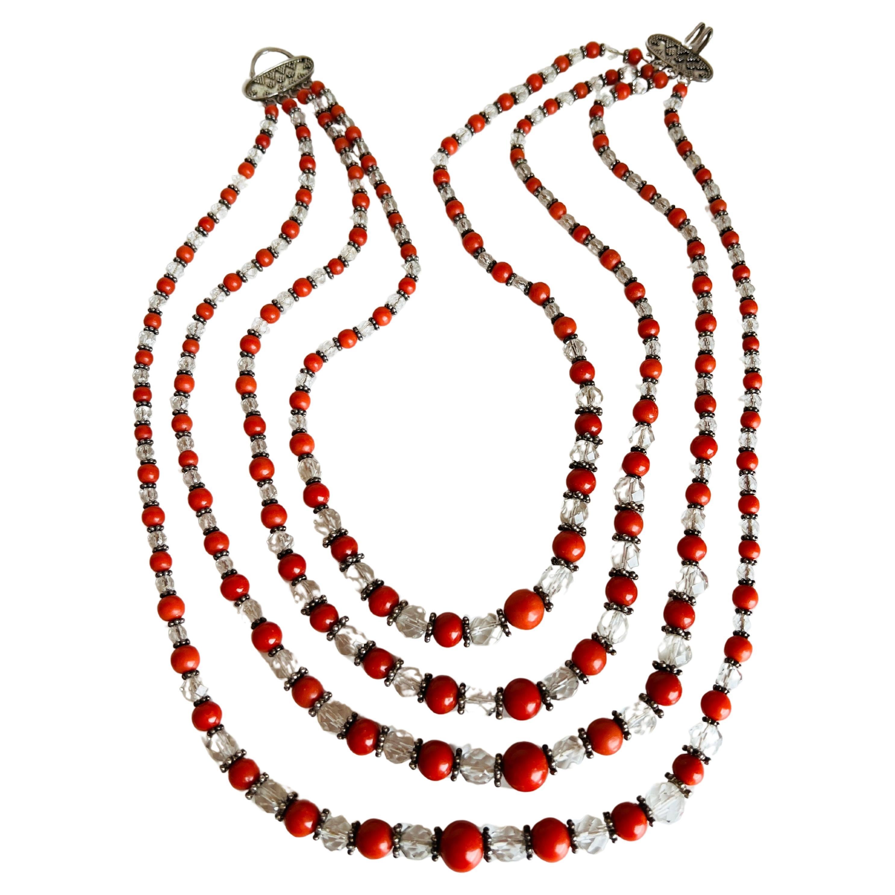 Eine elegante Halskette mit 4 Strängen aus abwechselnd leuchtenden, orangeroten Korallenperlen und funkelnden, facettierten, klaren Glasperlen, die in ihrer Größe variieren, um den Reiz zu erhöhen. Die Fassung aus Sterlingsilber sorgt für ein