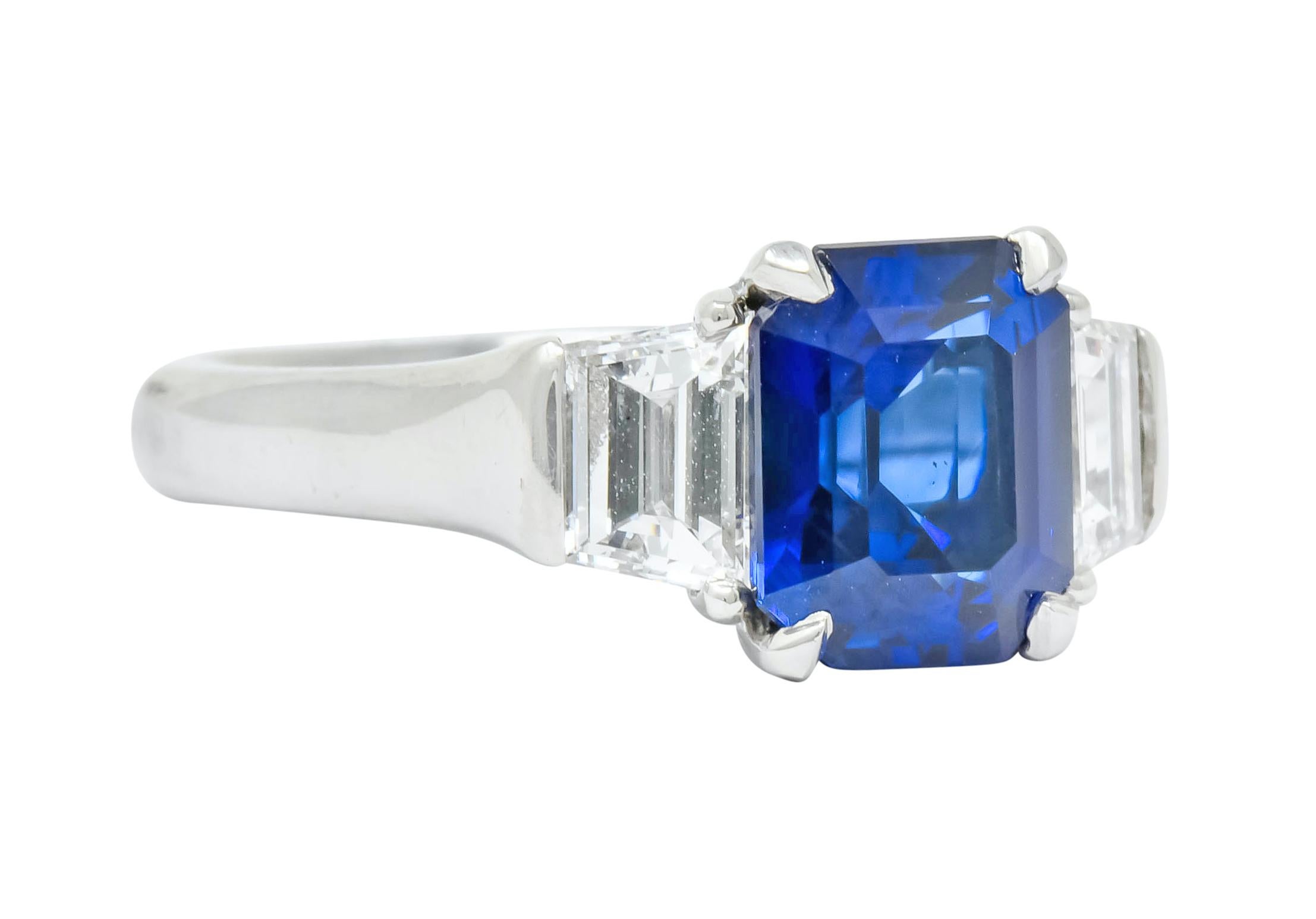 Centering an emerald cut sapphire weighing approximately 3.00 carats, transparent medium-dark royal blue in color

Flanked by two trapezoid cut diamonds weighing in total 1.02 carats; very well-matched G/H color with VVS clarity

Maker's mark and