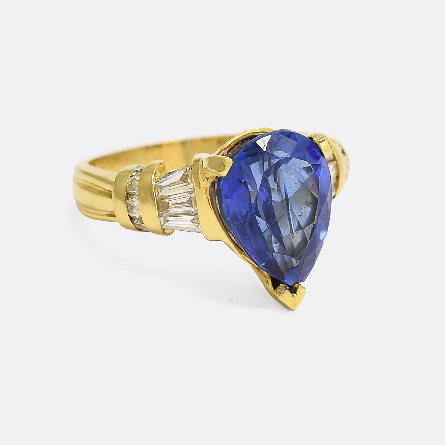 An eye-catching tanzanite solitaire ring dating from the 1980s. The shoulders are set with tapered baguette cut diamonds and a row of tension set brilliant cuts, and the principal pear cut stone displays a stunning vibrant purplish blue. Crafted in