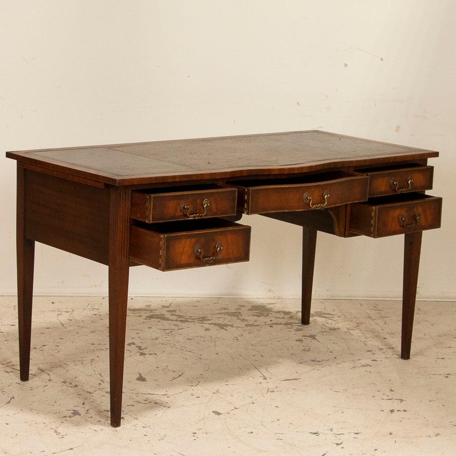 Distinctive and elegant, this English mahogany writing desk has 5 functioning drawers in addition to two unique 