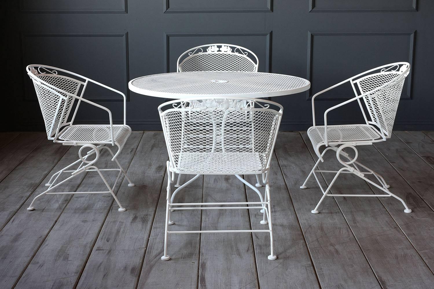 This 1960s five-piece outdoor dining set includes a dining table and four armchairs made of iron finished in an off-white color. The dining table features a classic design with a pedestal base and a mesh wire top with an umbrella stand in the