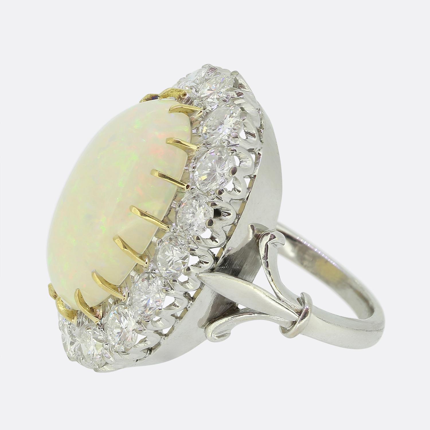 Ecco uno squisito anello da abito con al centro un grande opale bianco che vanta un ipnotico gioco di colori, tra cui sprazzi di arancione e verde. La pietra principale è circondata da un'aureola di diamanti tondi brillanti bianchi, disposti