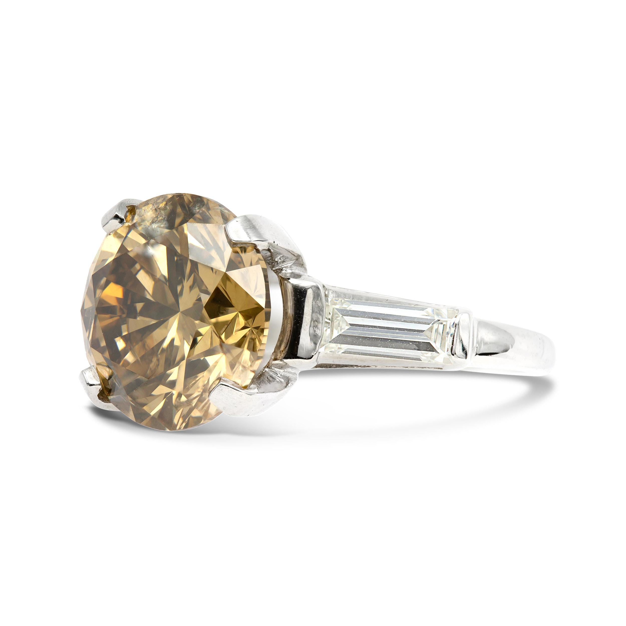 Where classic meets unconventional, this impressive 5.35 carat Fancy Yellow-Brown centered ring is a complete dream. The warm cognac colored diamond is set in a four-prong basket, accented by two sleek straight baguettes set in platinum. This ring