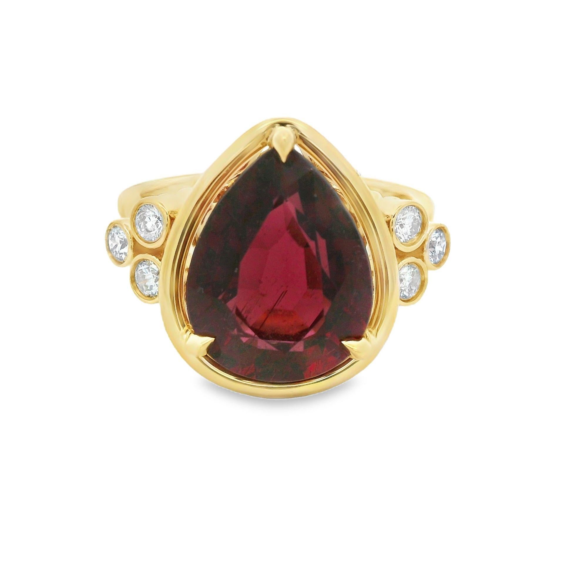 Crafted in 18 karat yellow gold, this exquisite ring features a stunning 5.49 carat pear-shaped tourmaline, rich in deep red hues that radiate warmth and elegance. The bold centerpiece is beautifully complemented by 0.22 carats of natural round
