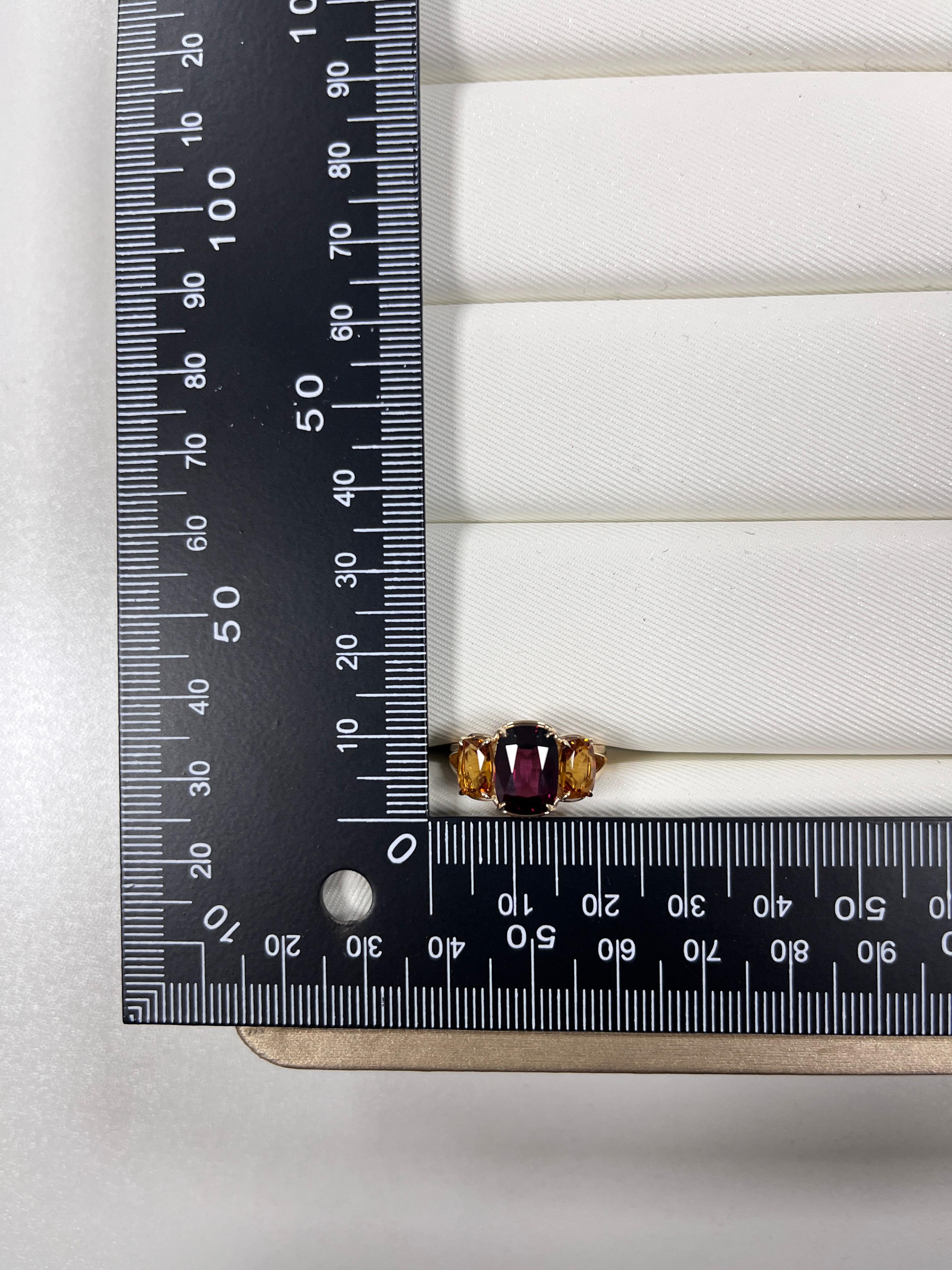 This radiant three-stone ring, expertly crafted in 14 karat yellow gold. At its center, a stunning 5.63-carat garnet captivates with its deep, fiery red hues, symbolizing passion and strength. Flanking the centerpiece, two vibrant citrine stones