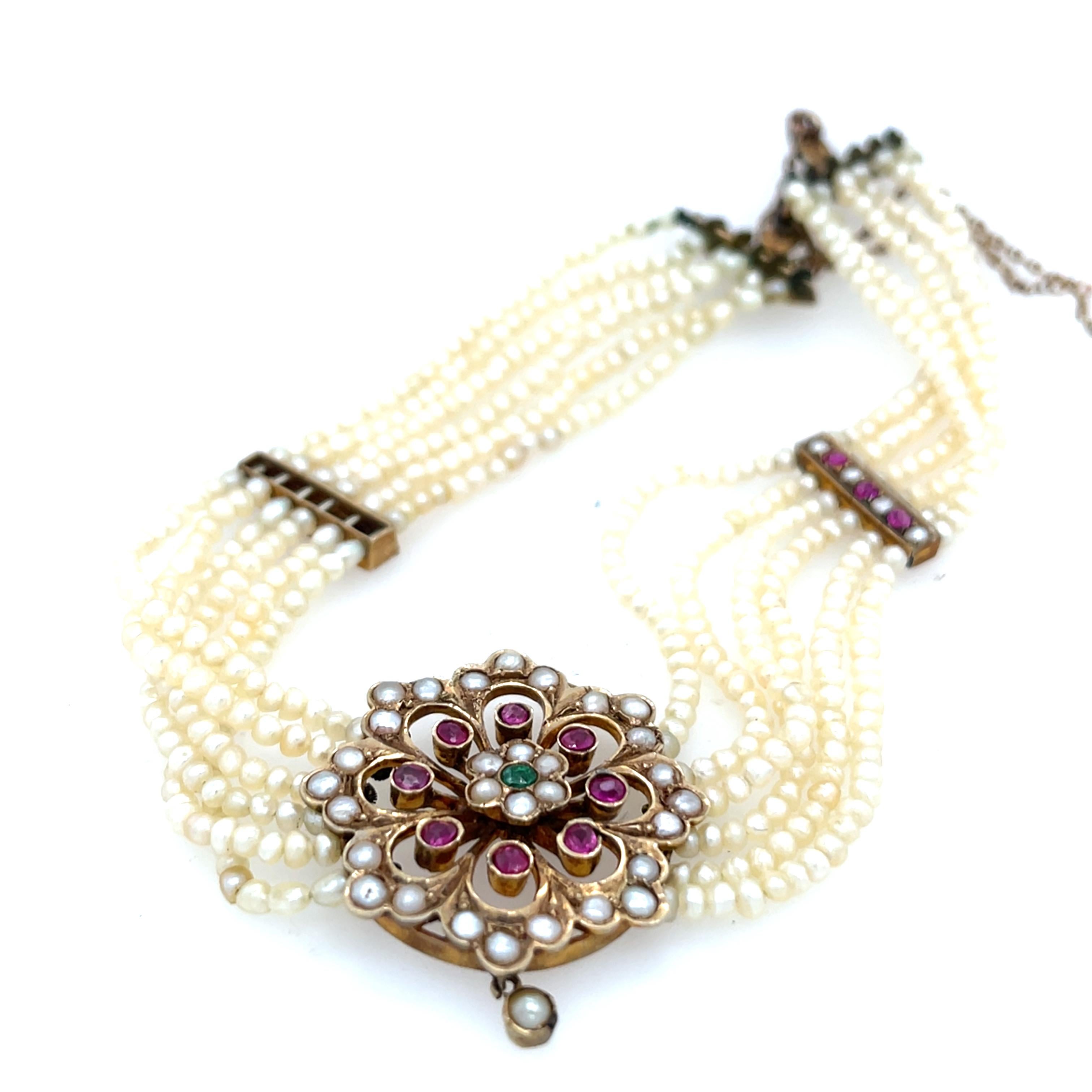 This vintage choker features six rows of lustrous 2.2mm seed pearls, highlighted by a vibrant emerald and ruby pendant, accented with additional seed pearls. Crafted in 9ct yellow gold, it combines timeless elegance with a pop of colour, making it