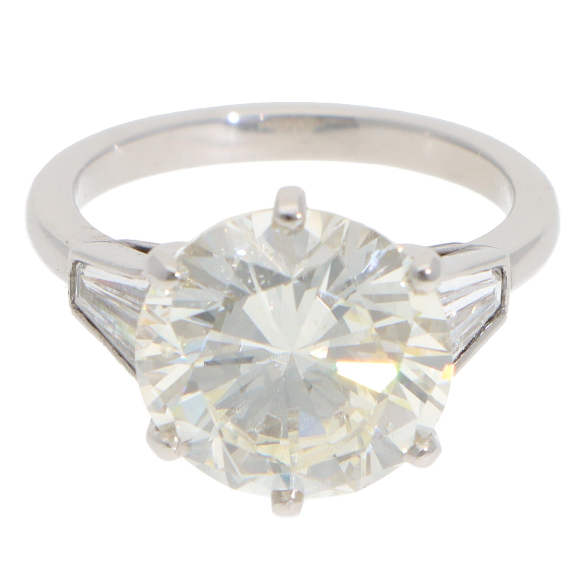 A breathtaking vintage 6.03ct diamond three-stone ring set in platinum.

The piece centrally features a magnificent round brilliant-cut diamond. The diamond is six-claw set to centre within an open back setting, which connects nicely to 2 trapezoid