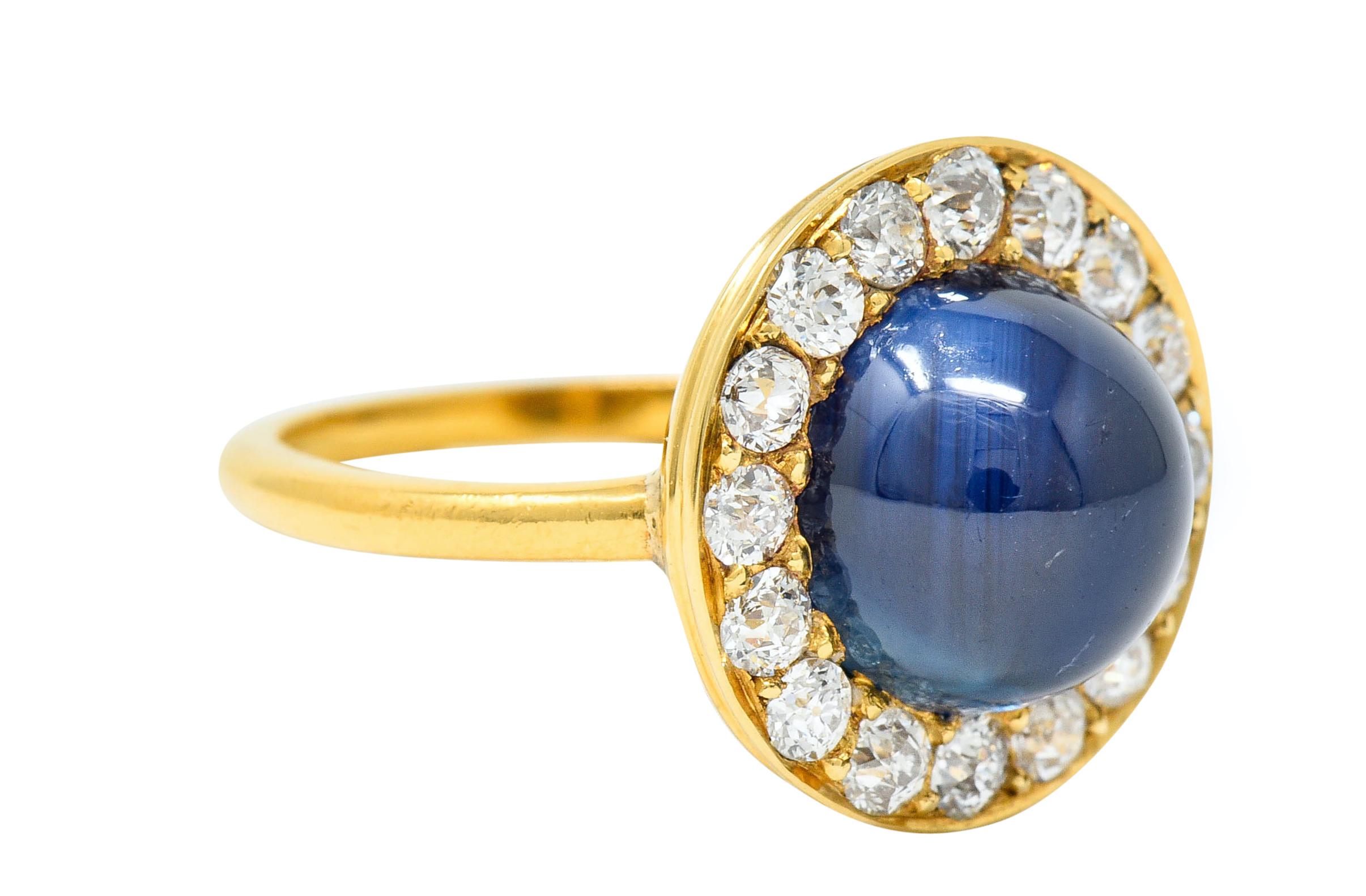 Circular cluster ring centers a round and highly domed sapphire cabochon weighing approximately 5.13 carats

Translucent dark blue in color with no indications of heat; Australian in origin

Surrounded by a halo of old European cut