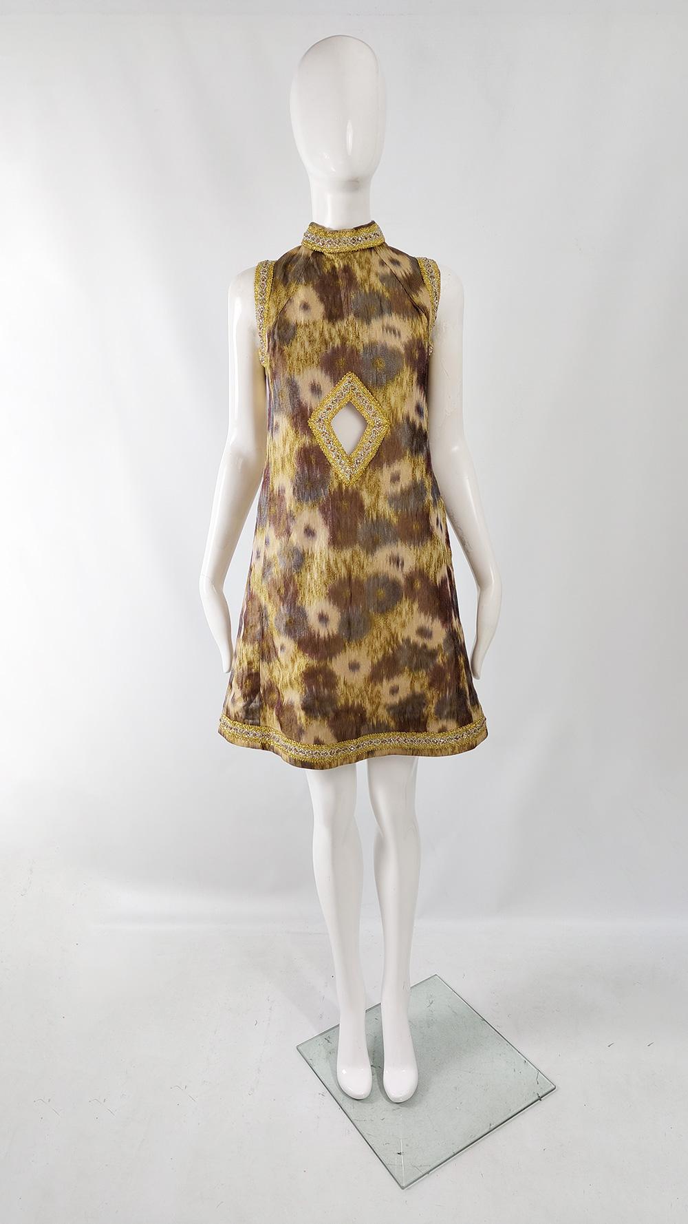 A stunning and rare vintage women's dress from the 60s. In a synthetic woven fabric that gives great structure, and has an Ikat style pattern woven throughout. The sleeveless armholes and mock neck are trimmed with a gold and silver lurex which is