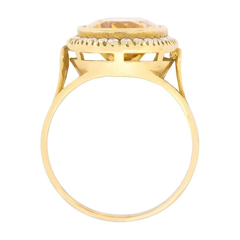 This vintage 1960s era citrine and diamond ring presents a 6.10 carat, rubover set, oval-shaped citrine amid a glittering single row halo comprised of round brilliant cut diamonds in 18 carat yellow gold. The round brilliant stones have an overall