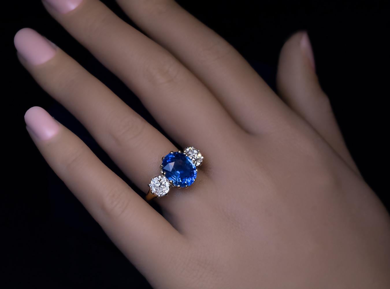 This classic three-stone engagement ring is crafted in 18K gold and platinum. The ring features an excellent natural unheated blue sapphire from Ceylon. The sapphire is flanked by two chunky pre-1900 old mine cut diamonds (I-J color, VS1