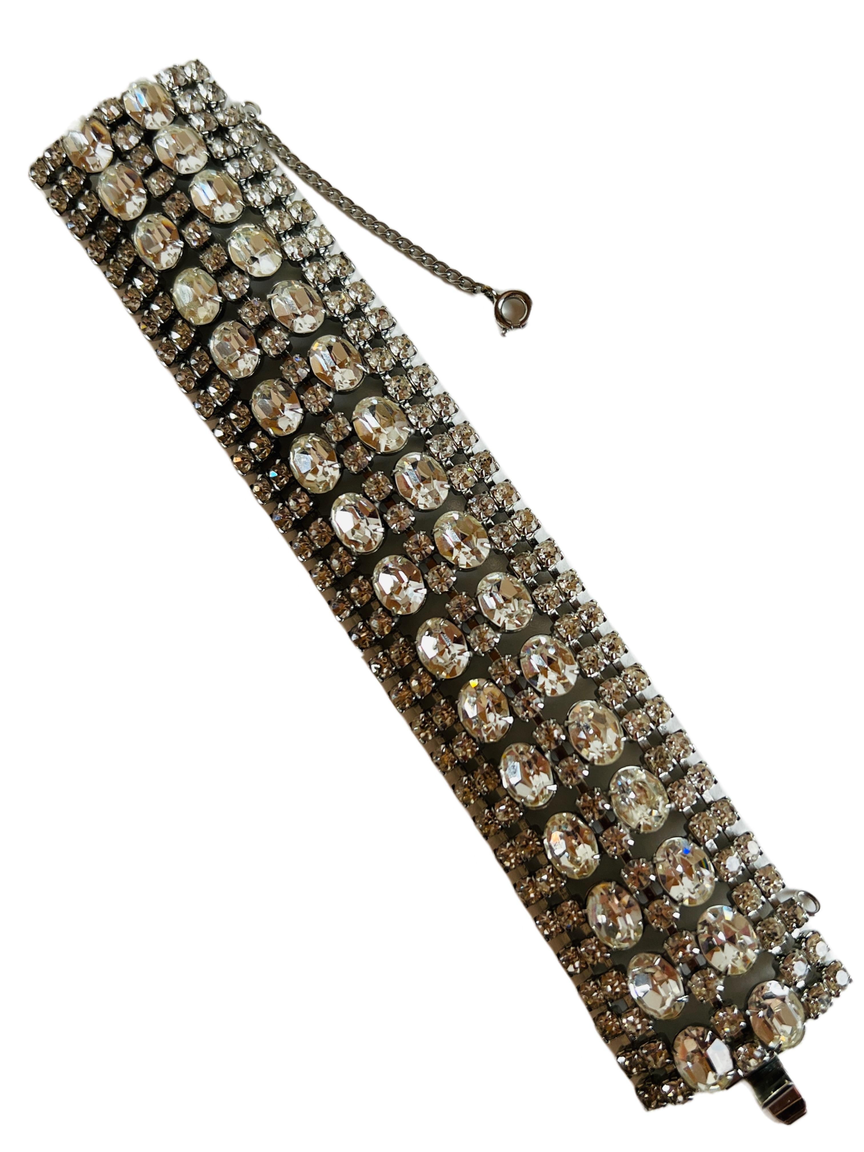 Opulent vintage bracelet, spanning seven rows wide and embellished with clear rhinestones, including both round and sizable oval cuts, all elegantly mounted in silver tone prong settings and enhanced with a safety chain for added security. Ideal for