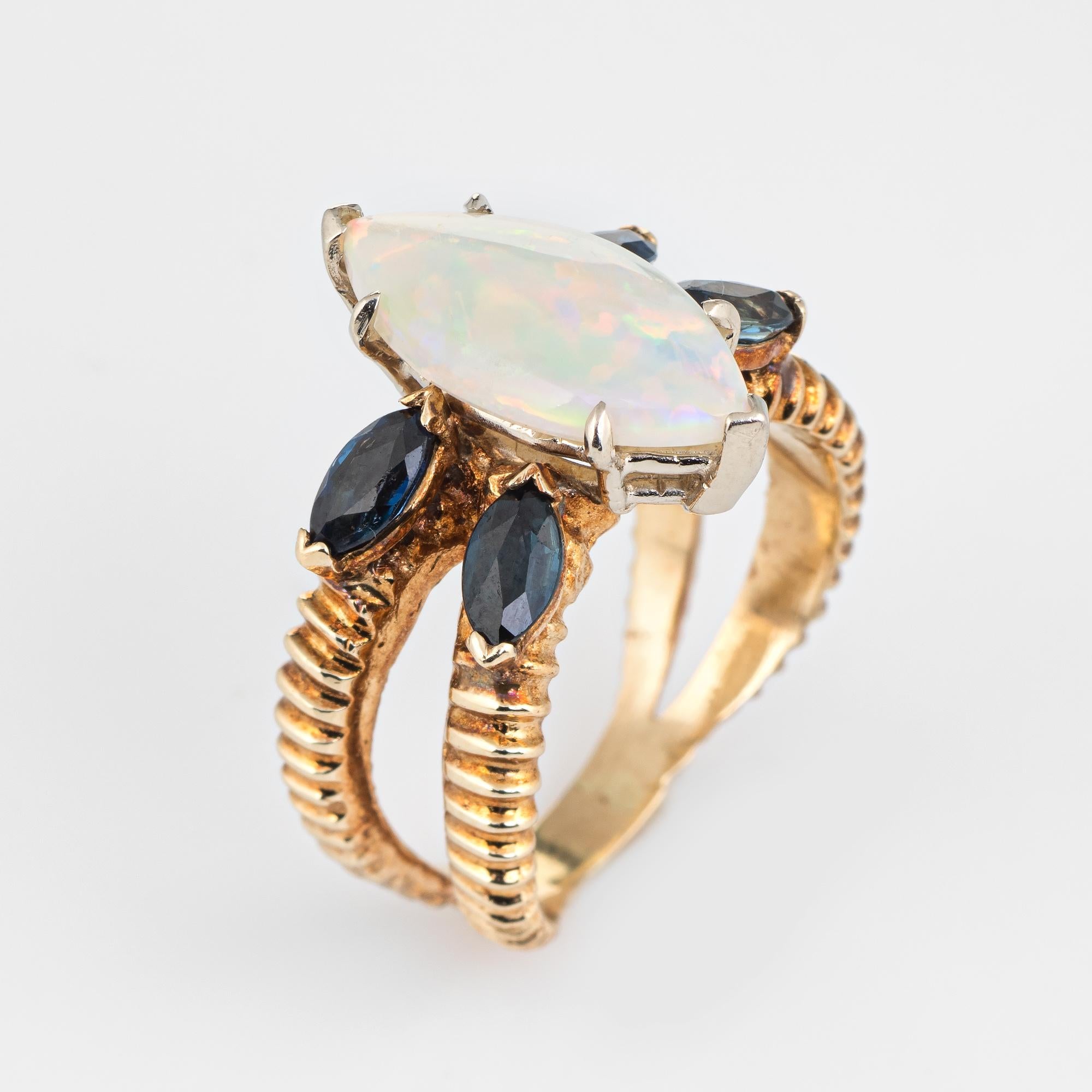 Stylish vintage opal & sapphire ring (circa 1970s) crafted in 14 karat yellow gold. 

Cabochon cut natural opal measures 15mm x 7.5mm (estimated at 3.50 carats), accented with four estimated 0.15 carat (each) marquise cut blue sapphire. The total