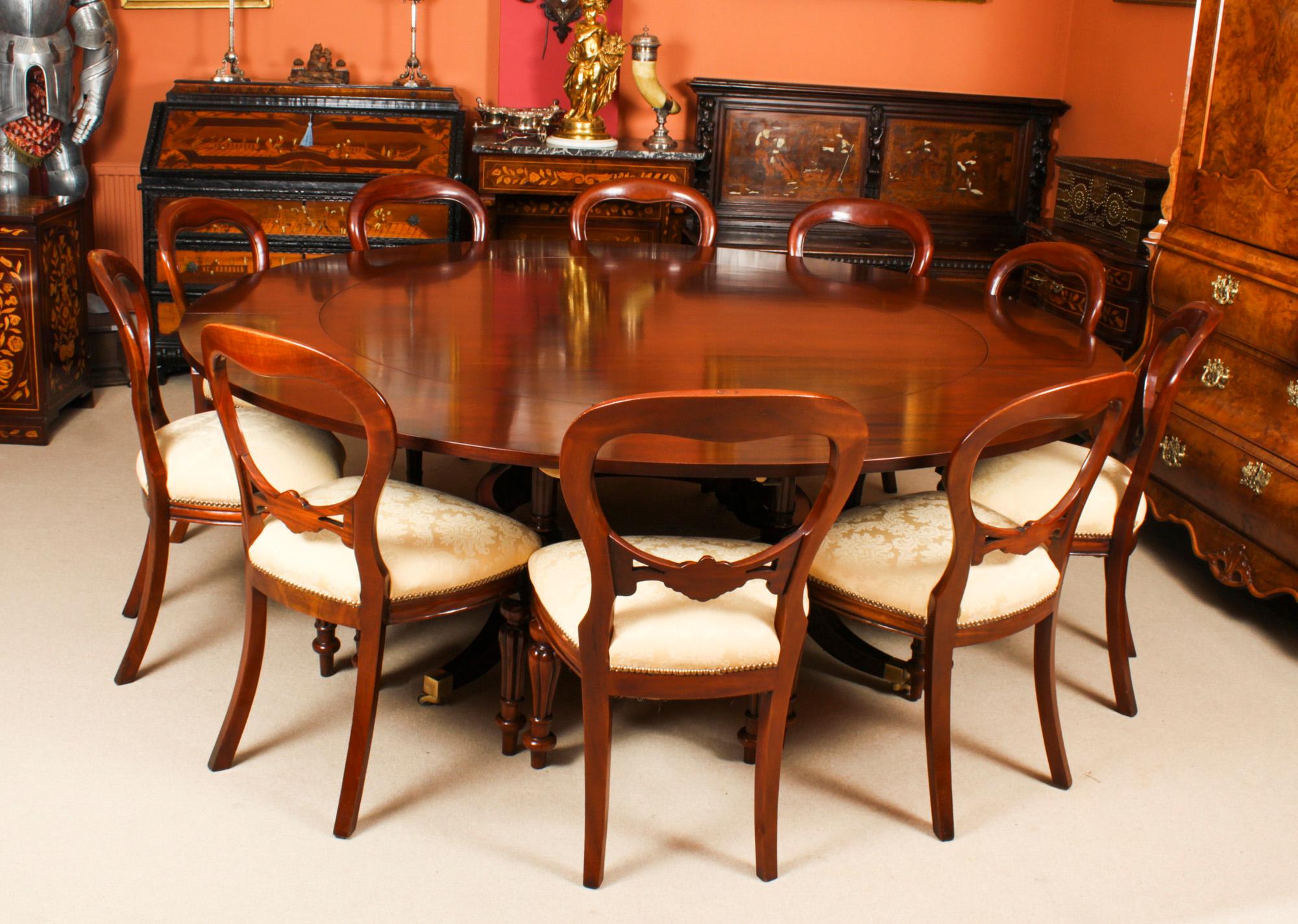 This is a beautiful Regency Revival Jupe style dining table and leaf holder by Arthur Brett, mid 20th Century in date.

The table has a solid mahogany top with five peripheral leaves that can be added around the circumference when required. It is