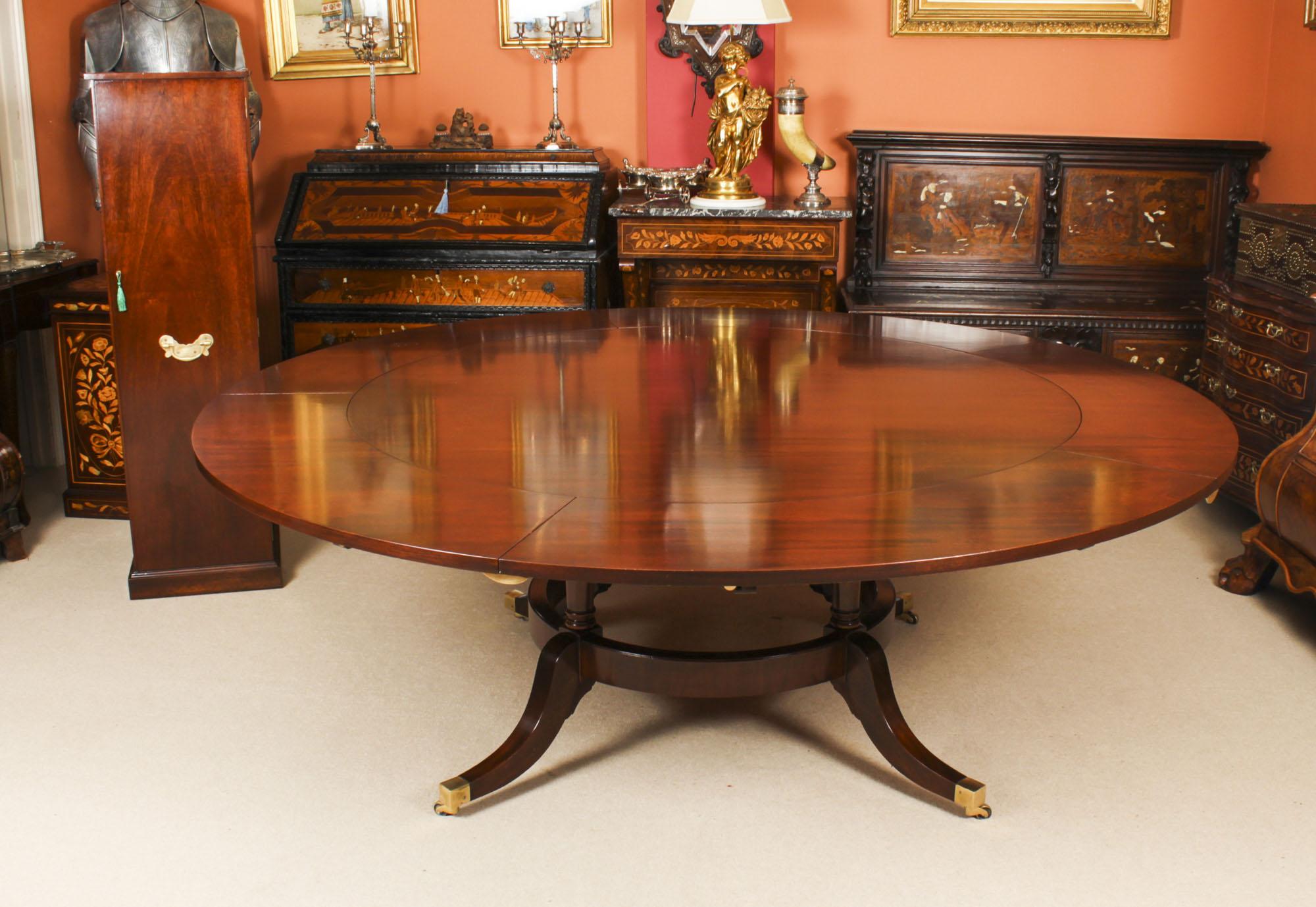 This is a beautiful Regency Revival dining set comprising a Jupe style dining table and leaf holder by Arthur Brett, and a set of ten balloon back dining chairs, mid 20th Century in date.

The table has a solid mahogany top with five peripheral