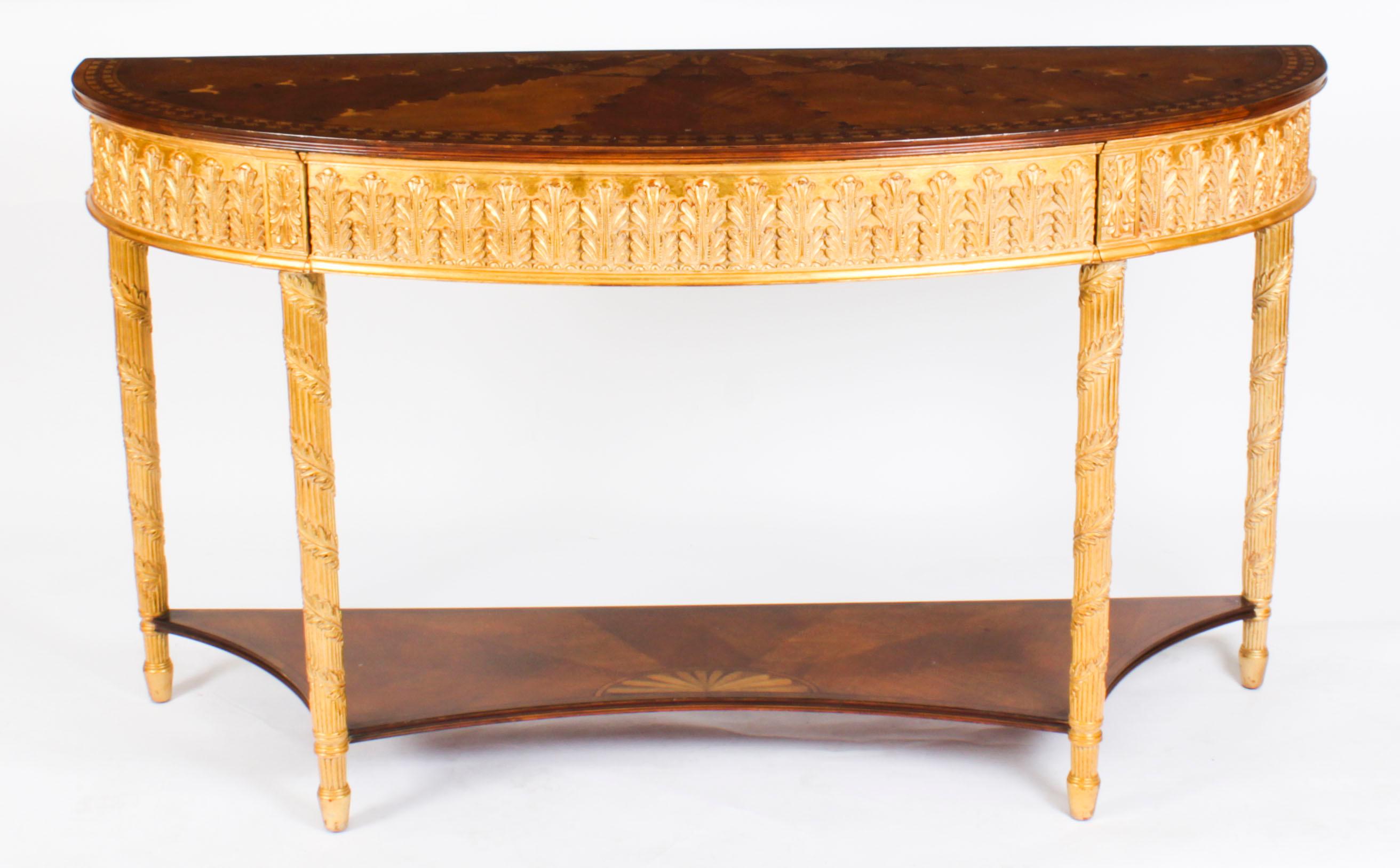 This is an elegant Vintage Sheraton Revival parcel gilt and marquetry console table dating from the second half of the 20th century.

This magnificent piece is crafted from walnut, the top is richly inlaid with a marquetry of flowerbells and