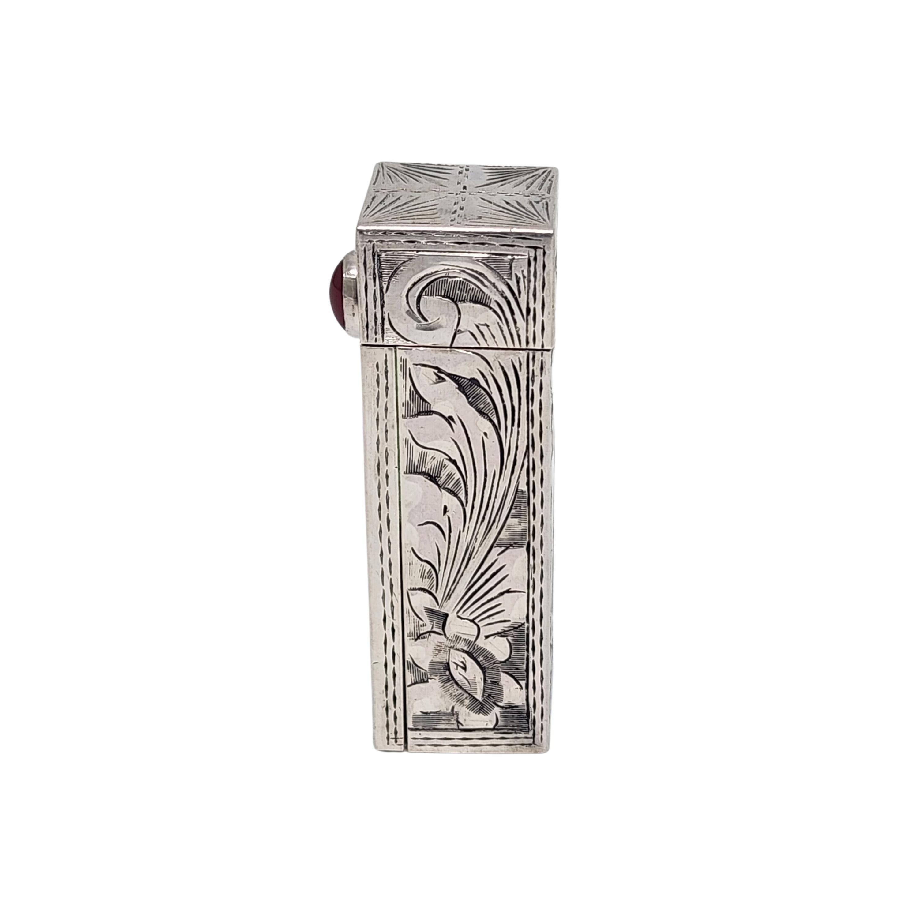 Vintage Italian 800 silver mirror lipstick case with red stone.

An etched flower and scroll design adorn this lipstick case that open to reveal a folding mirror. The oval red cabochon stone pushed up the lipstick and keeps the case folded when
