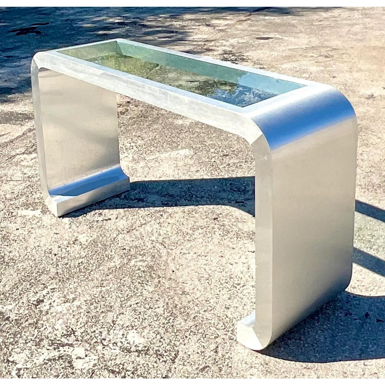 Fantastic vintage 80s console table. A chic waterfall design in a brushed chrome look. Tall in size with an inset glass panel on top. Acquired from a Palm Beach estate.