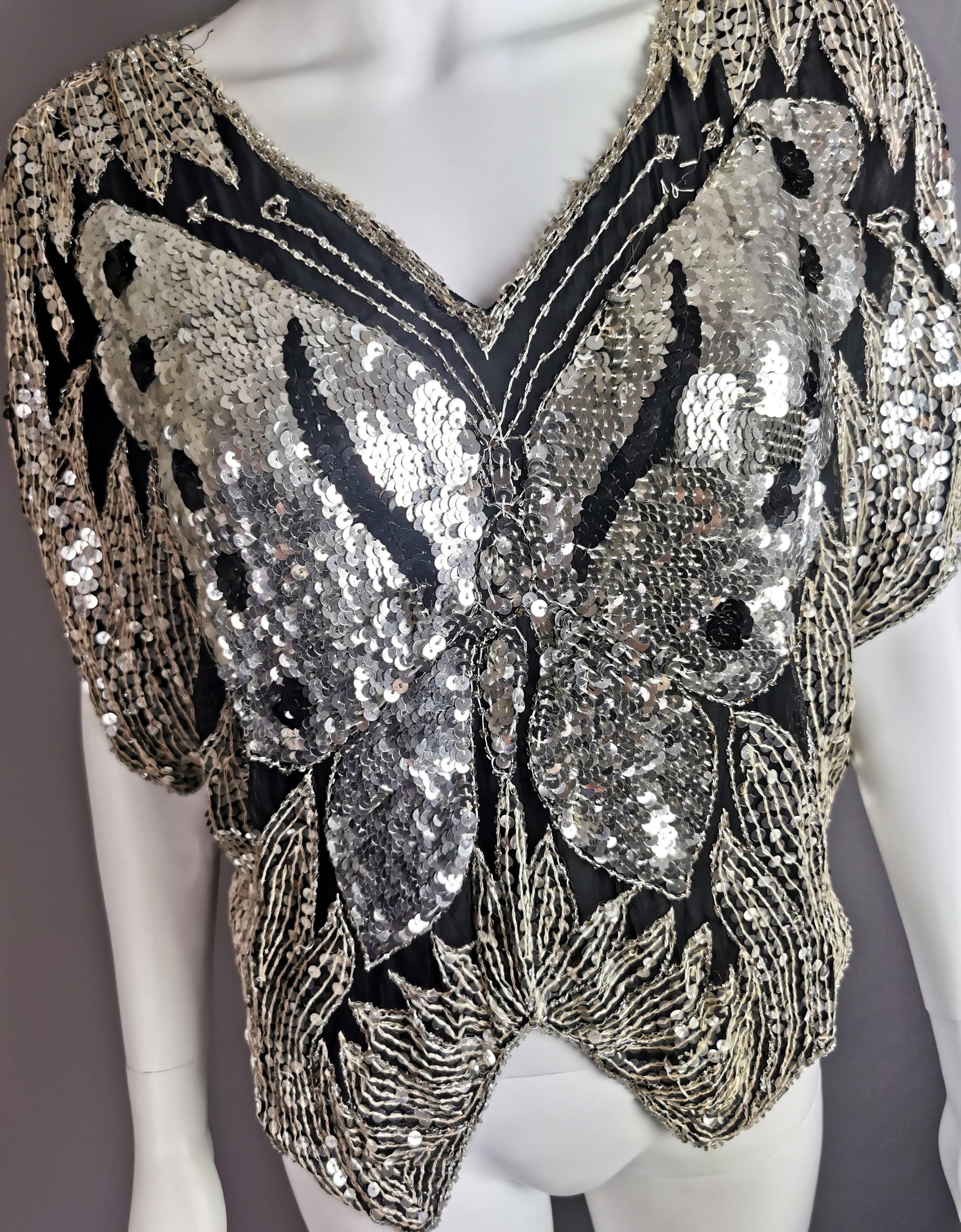 This 1980s sequin butterfly top has it all going on!

This amazing top is made from fine lightweight silk and adorned all over with sequins and beadwork in silver and black.

It has batwing type sleeves and the pattern on the top makes up a
