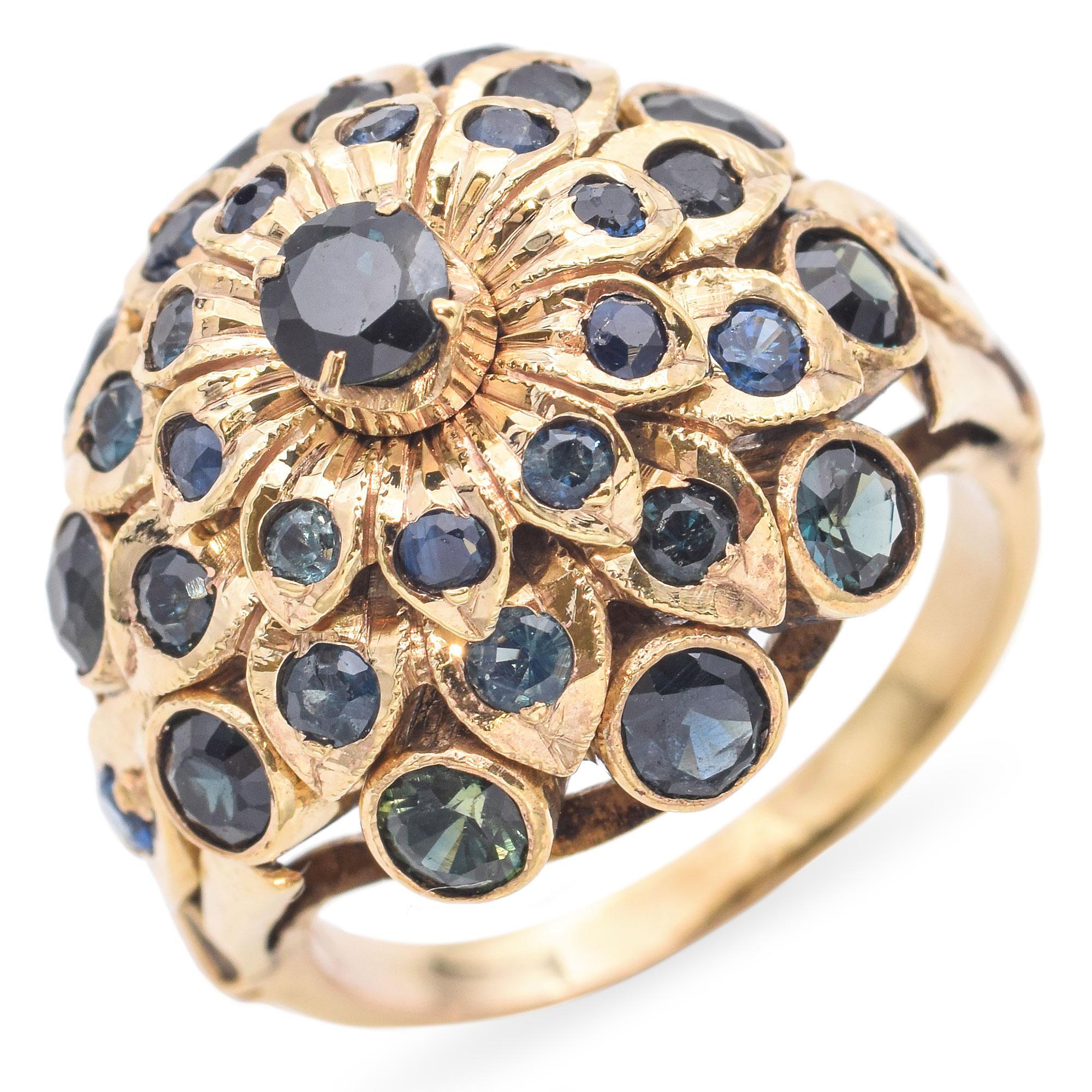 Cette bague de déclaration vintage est fabriquée en or jaune 8k riche et dispose d'un saphir vibrant à son centre, entouré de détails floraux complexes et une multitude d'autres melee. Ce design audacieux est à la fois romantique et royal, la pierre