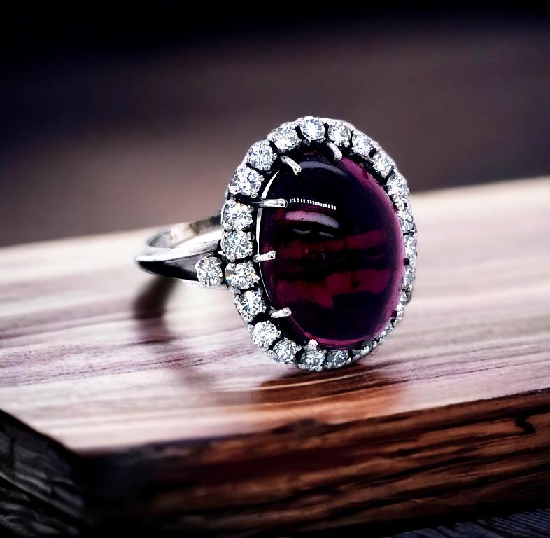 Vintage cabochon garnet with an estimated weight of over 9 carat, with a crown-like halo diamonds 24 stones round brilliant cut with a total estimated weight of over 0.61 carat, on a tapered split shank. All set in 18 karat white gold. 

We believe