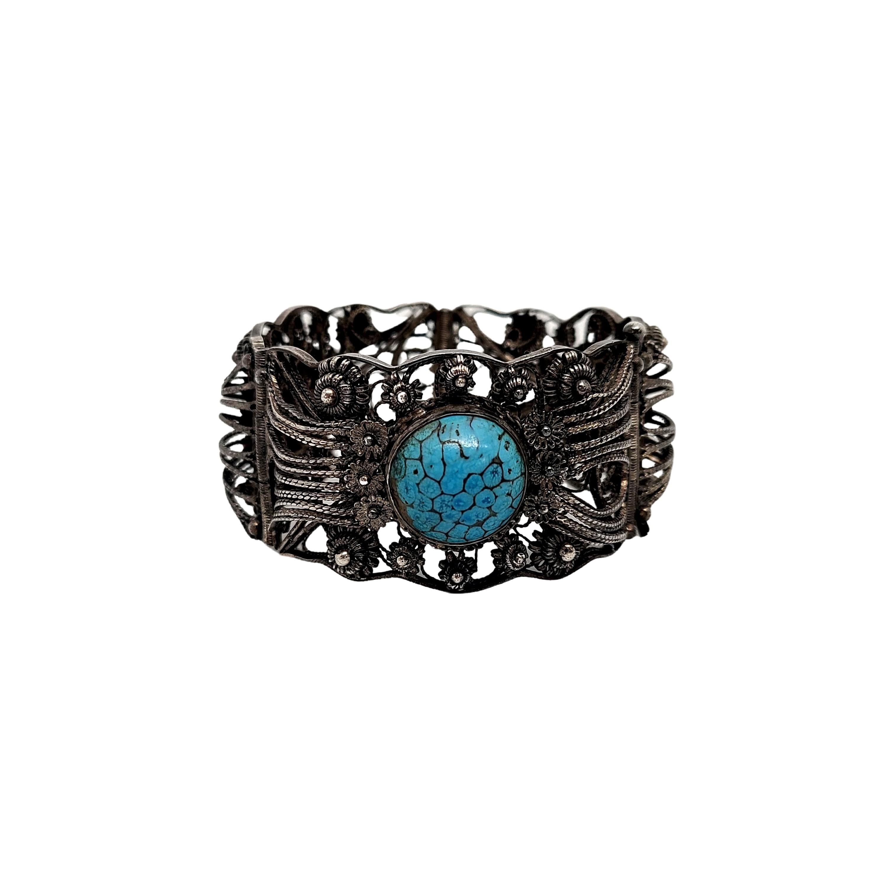900 silver filigree and turquoise panel bracelet.

3 panel bracelet featuring intricate filigree design and a round turquoise stone with blue and gray veining bezel set at the center of each panel. Pull pin closure.

Measures approx 7