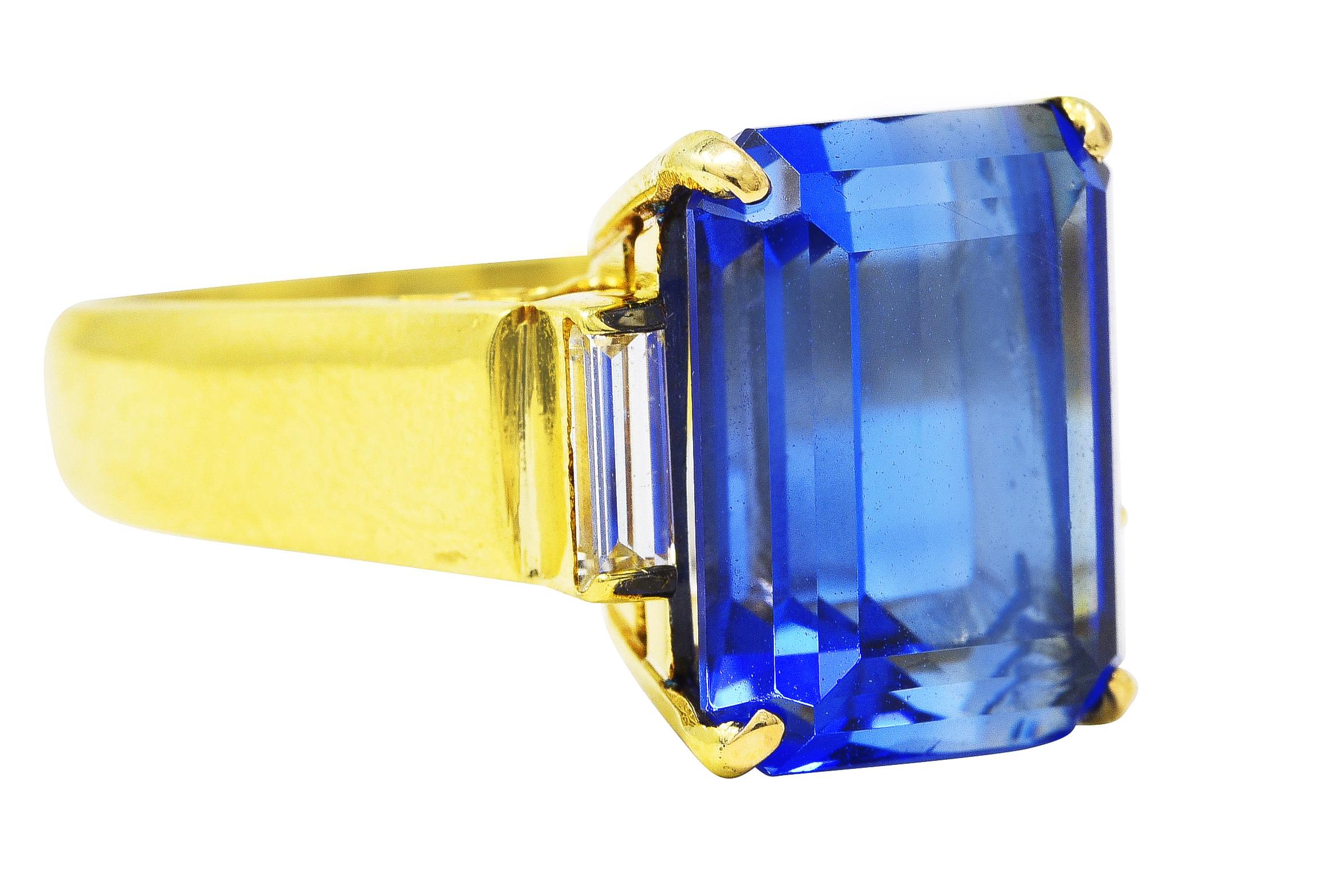 Substantial gemstone ring features an emerald cut tanzanite weighing approximately 8.85 carats. Basket set with eye clean violetish blue color - medium saturation. Flanked by cathedral shoulders accented by bar set baguette cut diamonds. Weighing in