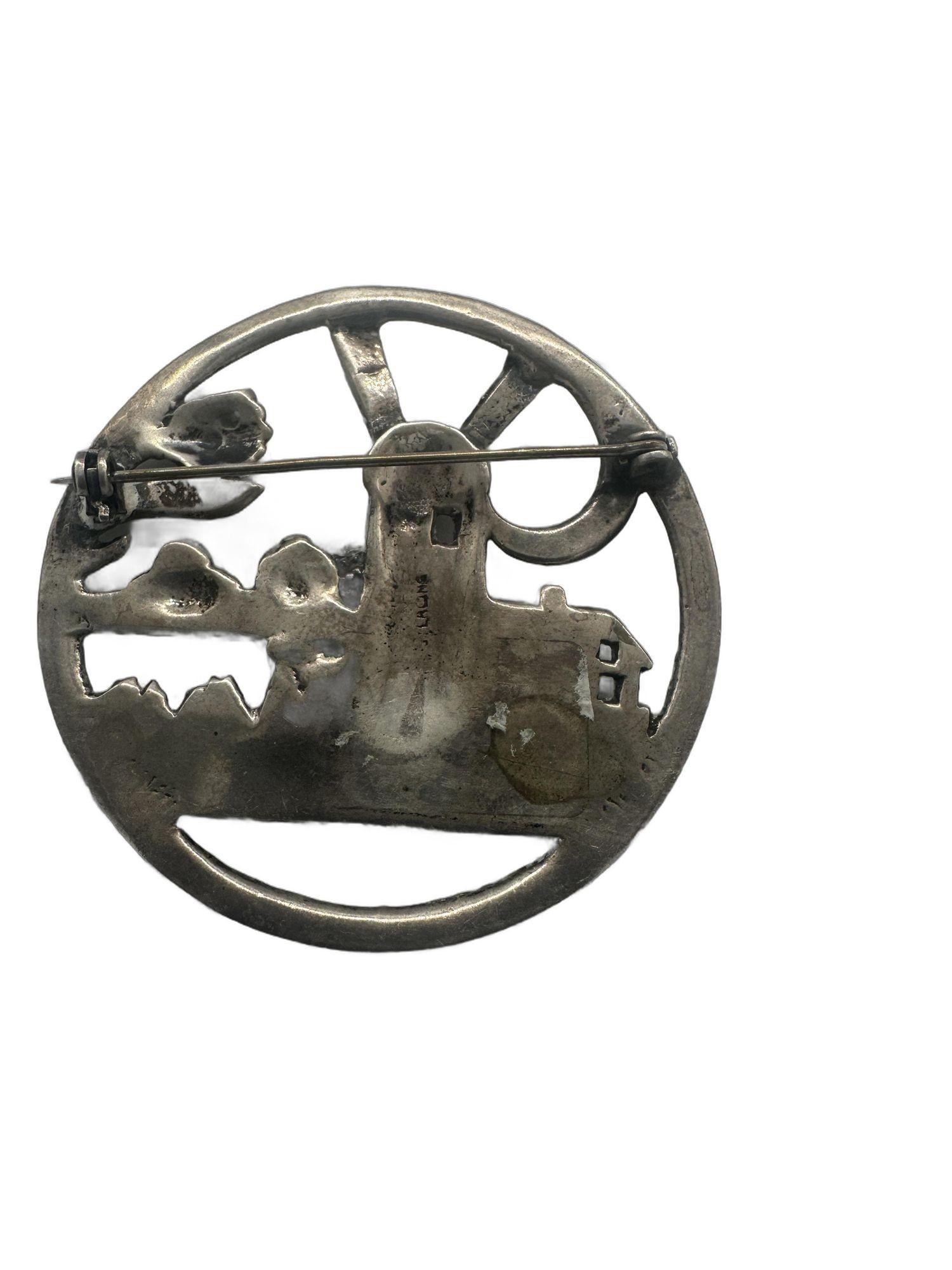 Diese Brosche aus 925er Sterlingsilber zeigt ein charmantes holländisches Windmühlendesign aus Delft, das mit floralen Akzenten verziert ist. Außerdem zeigt es eine ruhige Landschaftsszene mit einem Bauernhof oder einer ländlichen Gegend mit üppigen